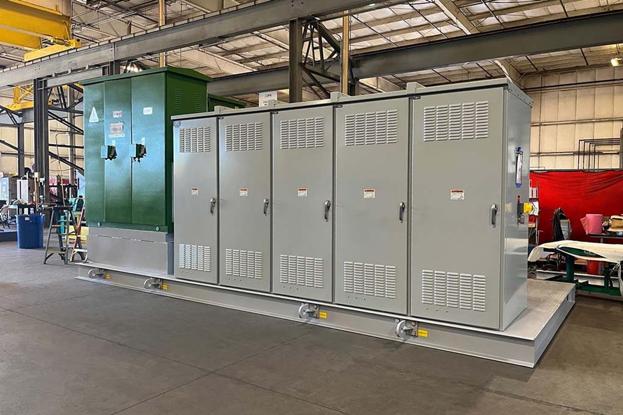 Industrial switchgear cabinets and a green transformer mounted on a skid in a service facility.