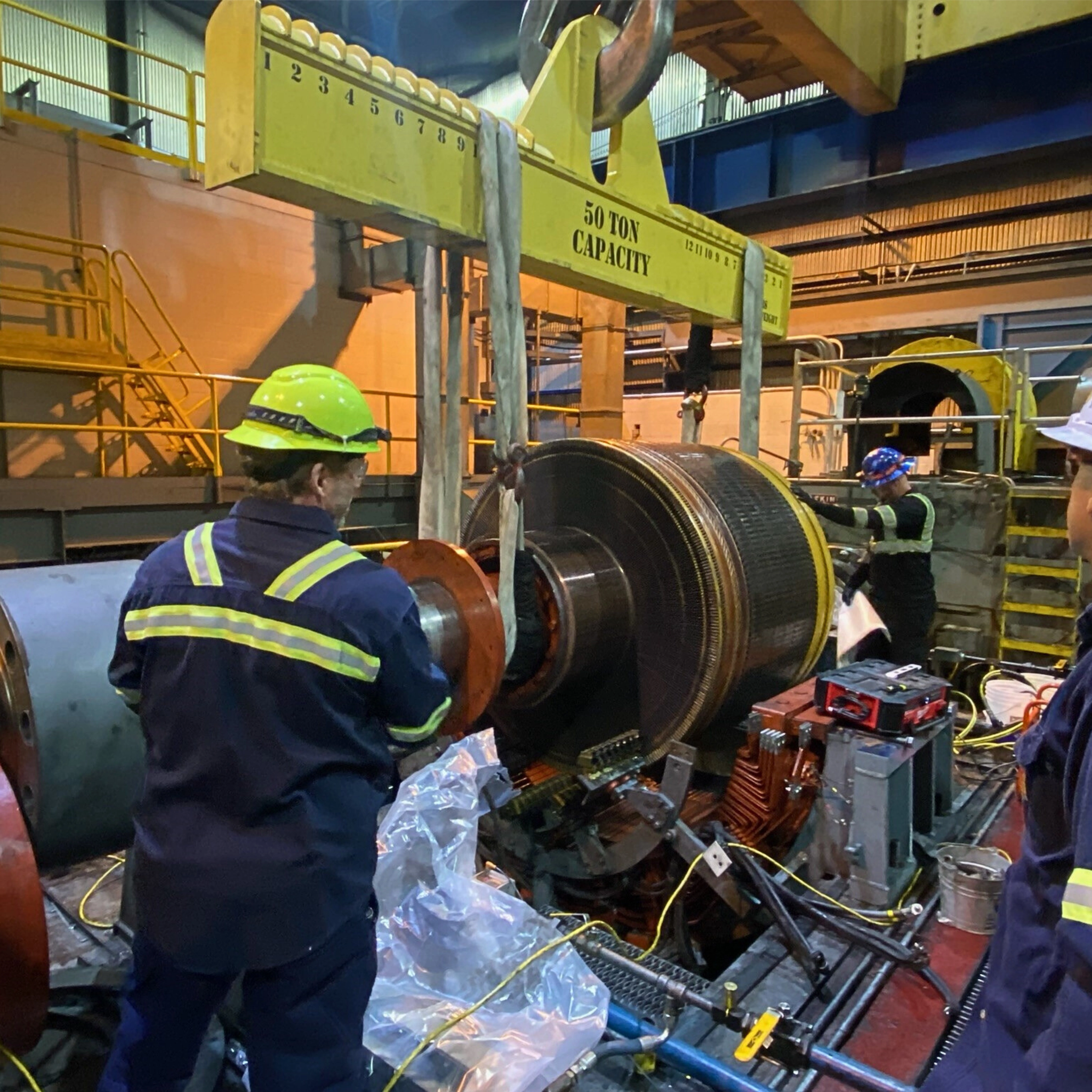 Technicians use a 50-ton crane to service a large generator rotor in an industrial facility.