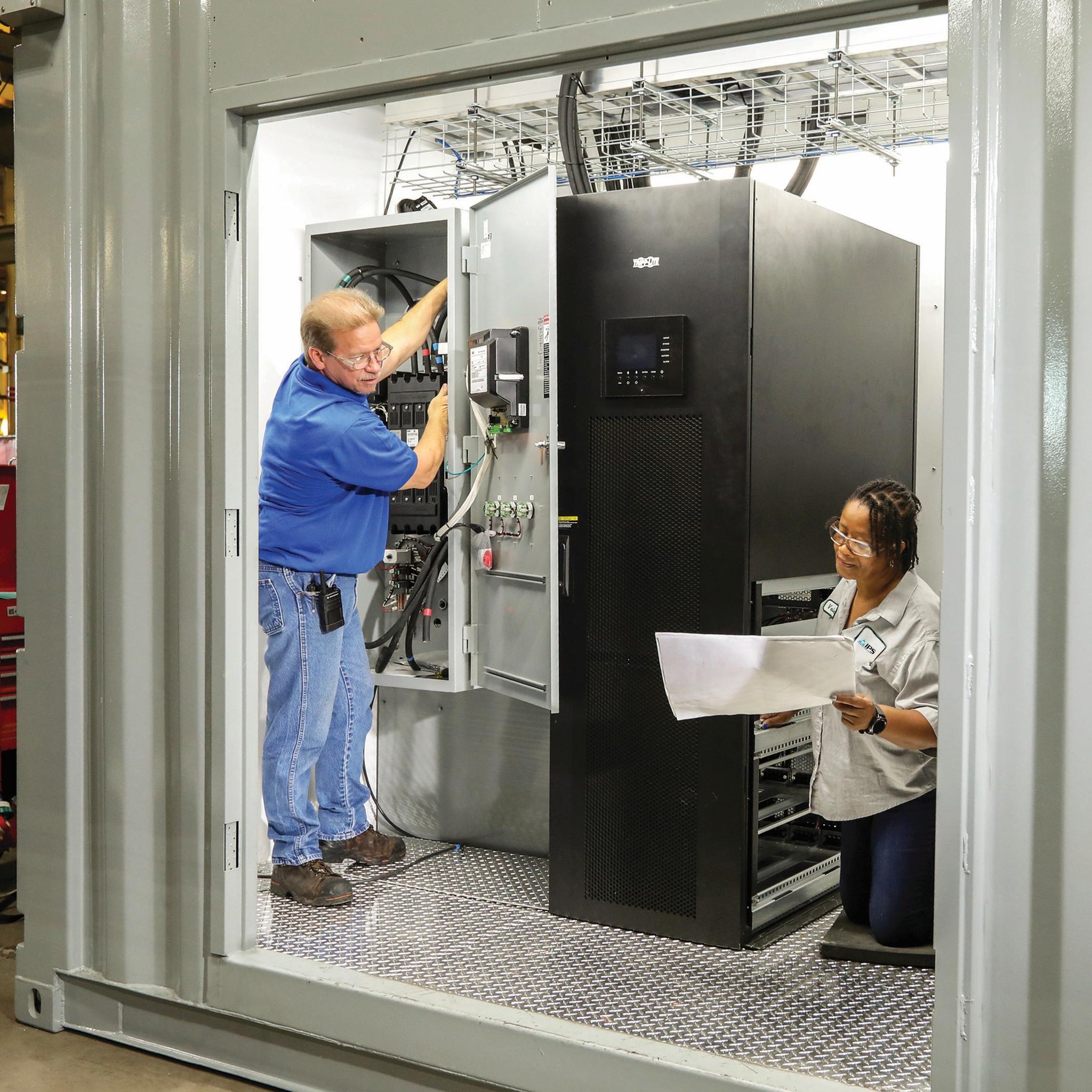 Technicians inspect an electrical control cabinet and review schematics beside industrial power equipment.