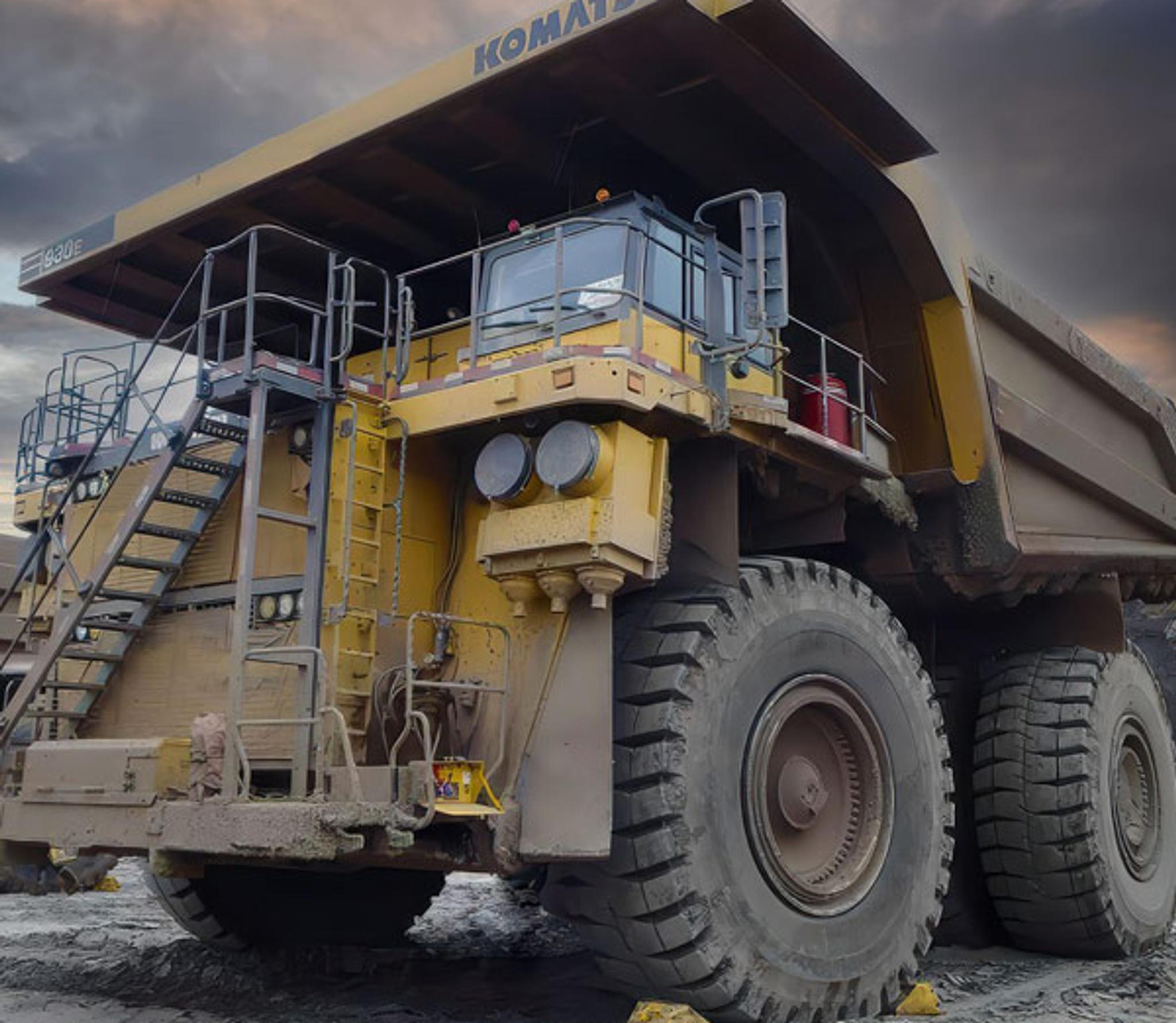 Camion-benne minier Komatsu géant stationné sur un chantier sous un ciel nuageux.