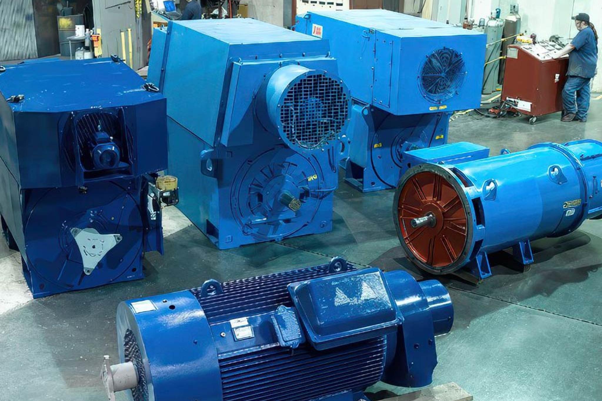 Moteurs et générateurs industriels bleus en atelier, avec un technicien au banc de commande.