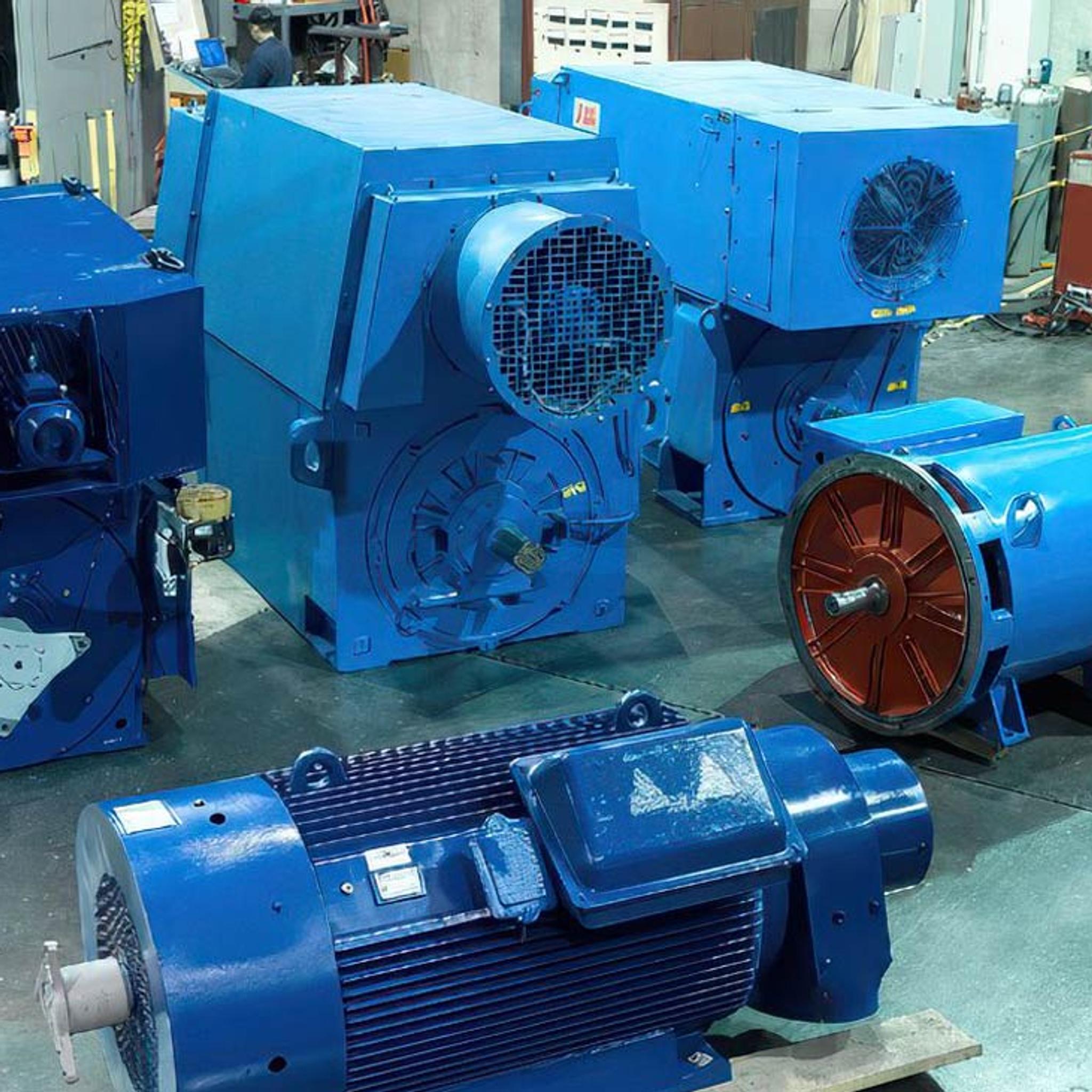 Moteurs et générateurs industriels bleus en atelier, avec un technicien au banc de commande.
