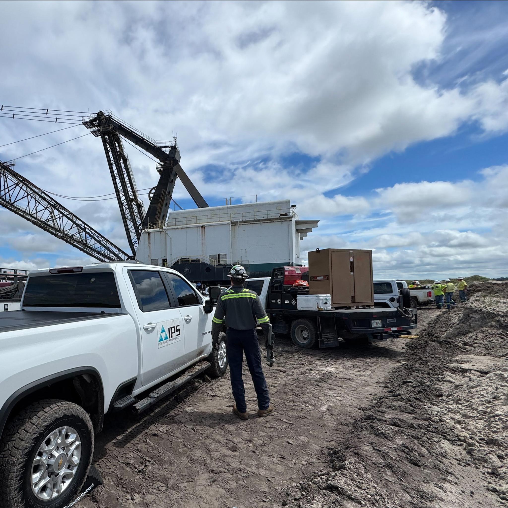 IPS technicians and service trucks support a large dragline at a muddy worksite.