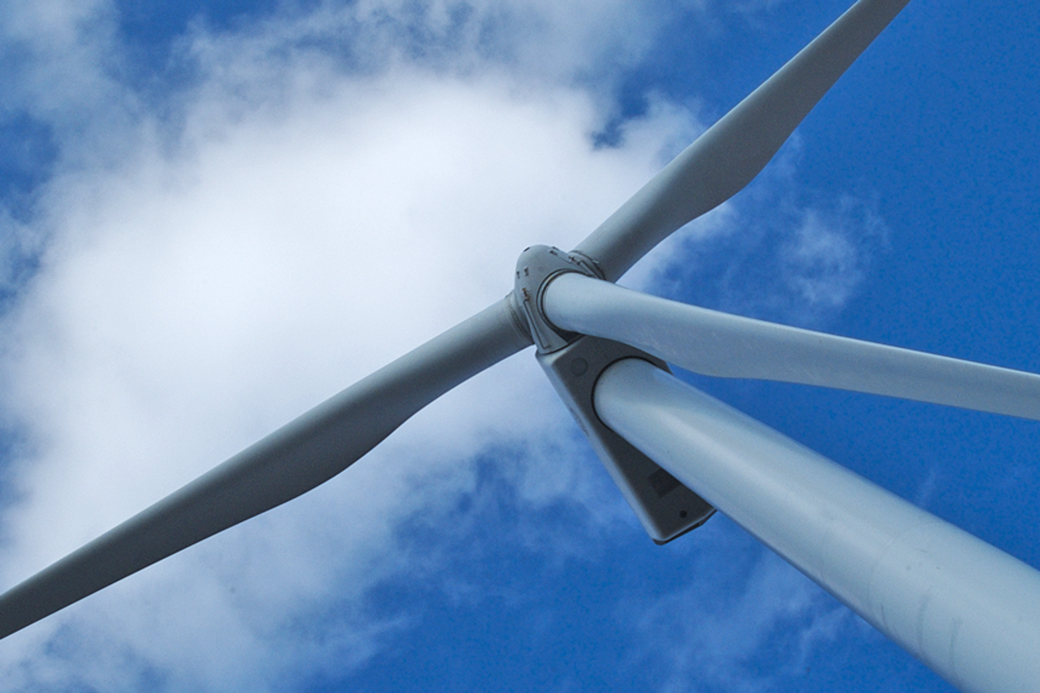 Éolienne à trois pales vue d’en dessous sur fond de ciel bleu nuageux.