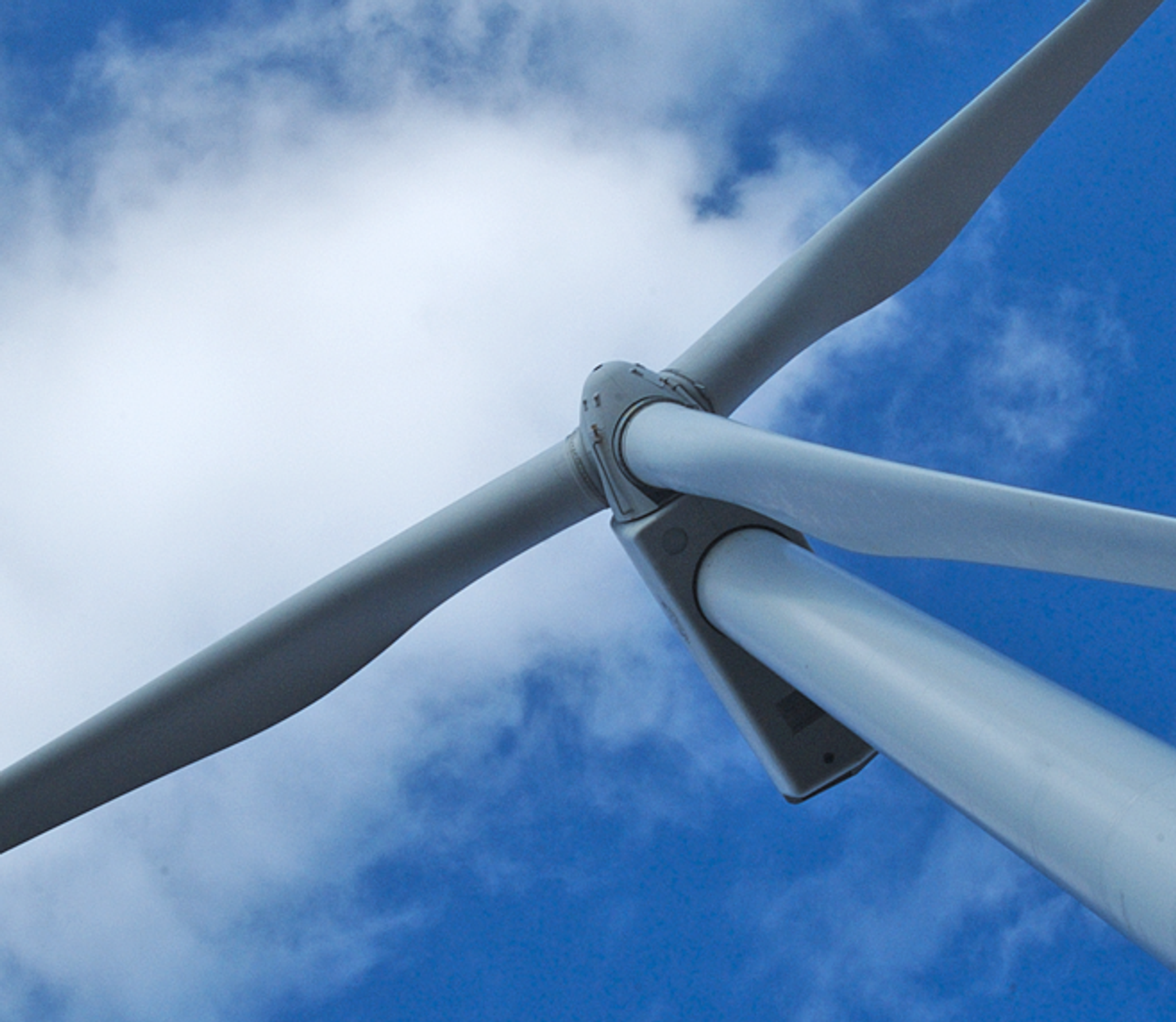 Éolienne à trois pales vue d’en dessous sur fond de ciel bleu nuageux.