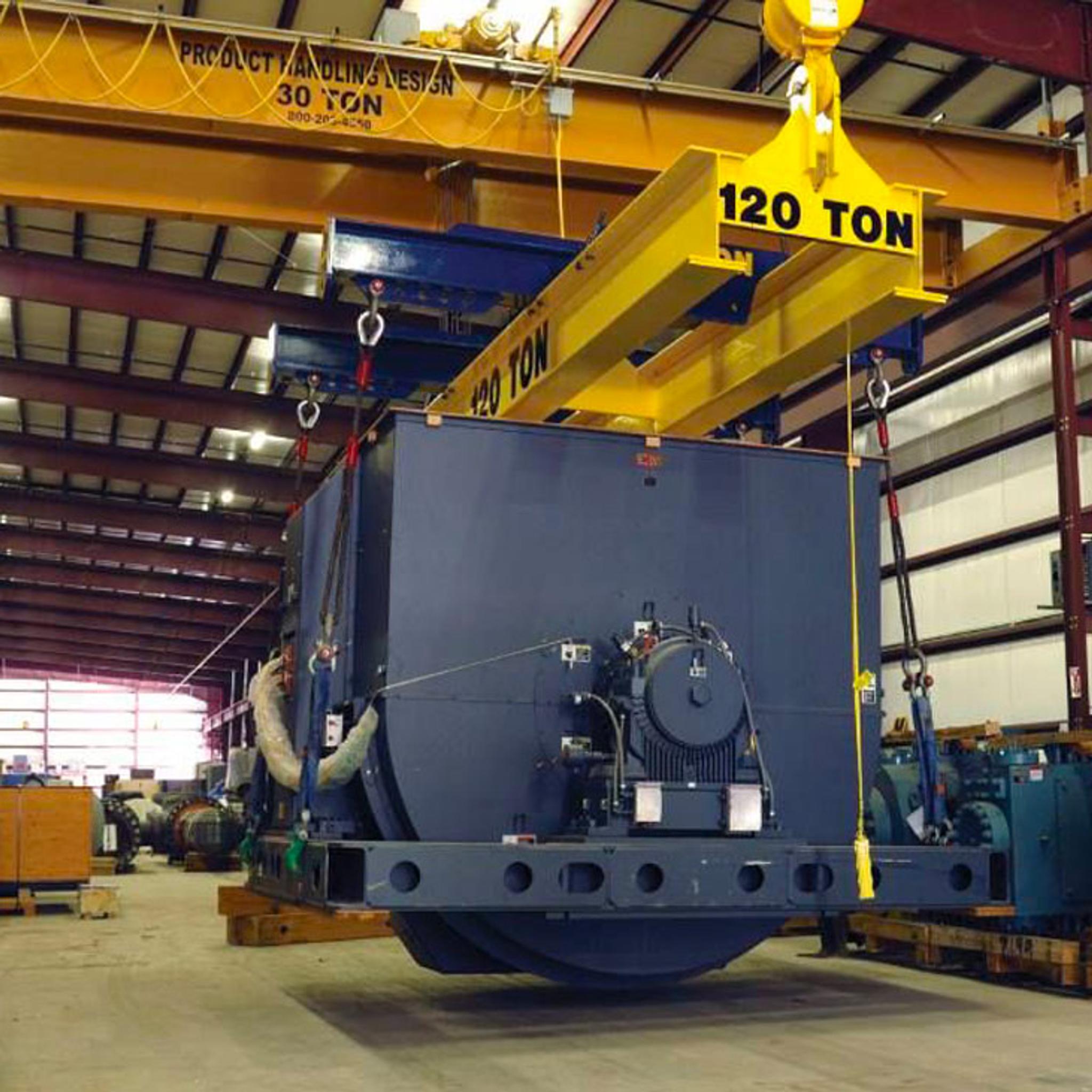 Un pont roulant de 120 tonnes soulève un grand équipement électrique dans un atelier industriel.
