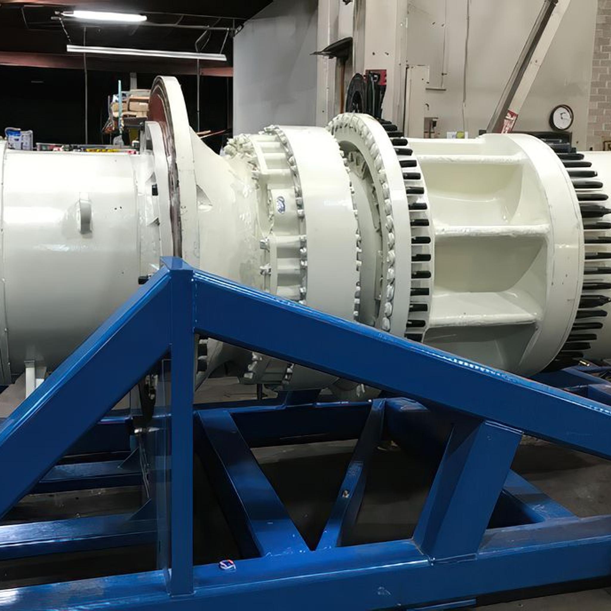 Large industrial generator rotor mounted on a blue steel service stand in a repair workshop.