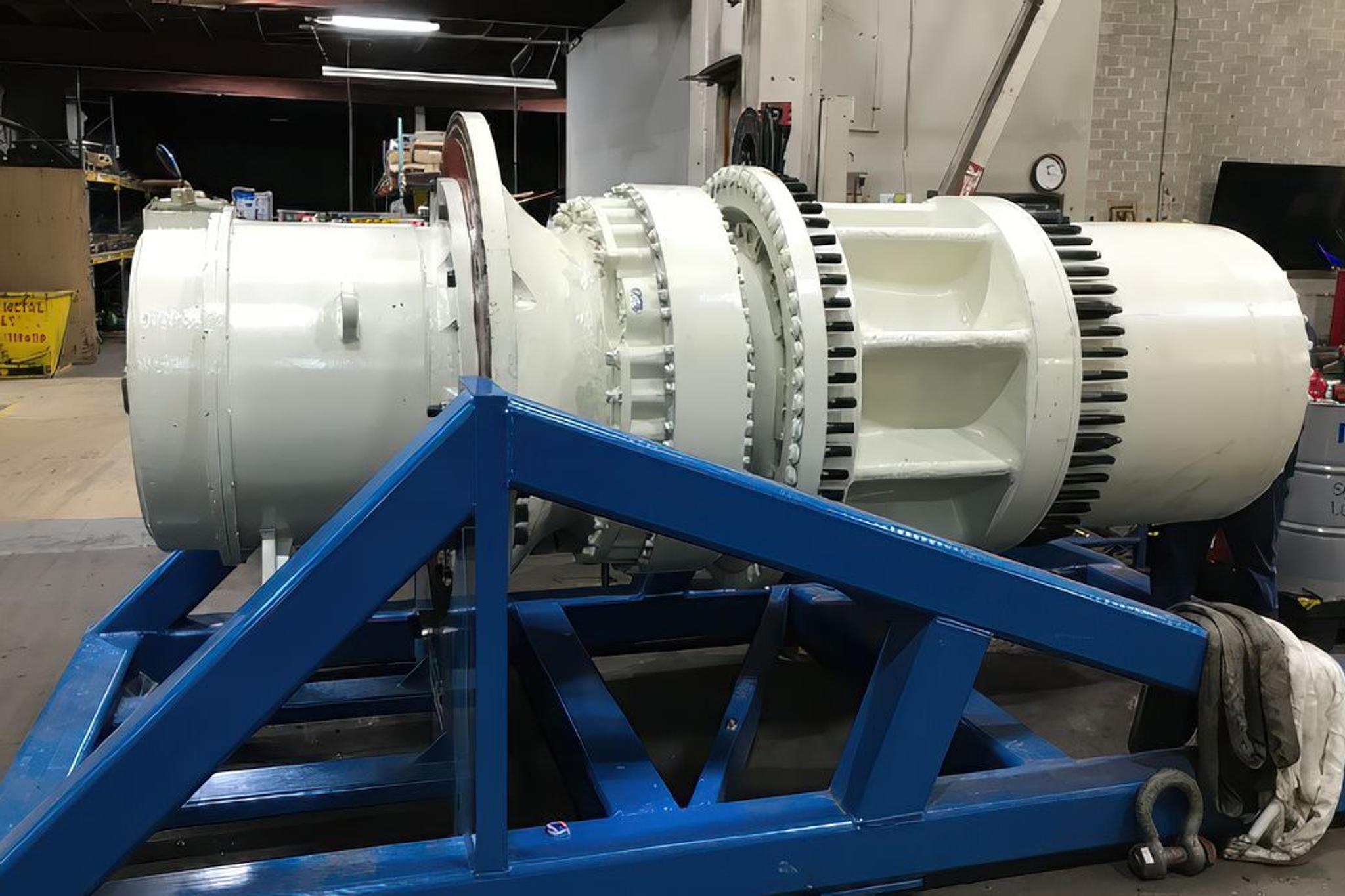 Large industrial generator rotor mounted on a blue steel service stand in a repair workshop.