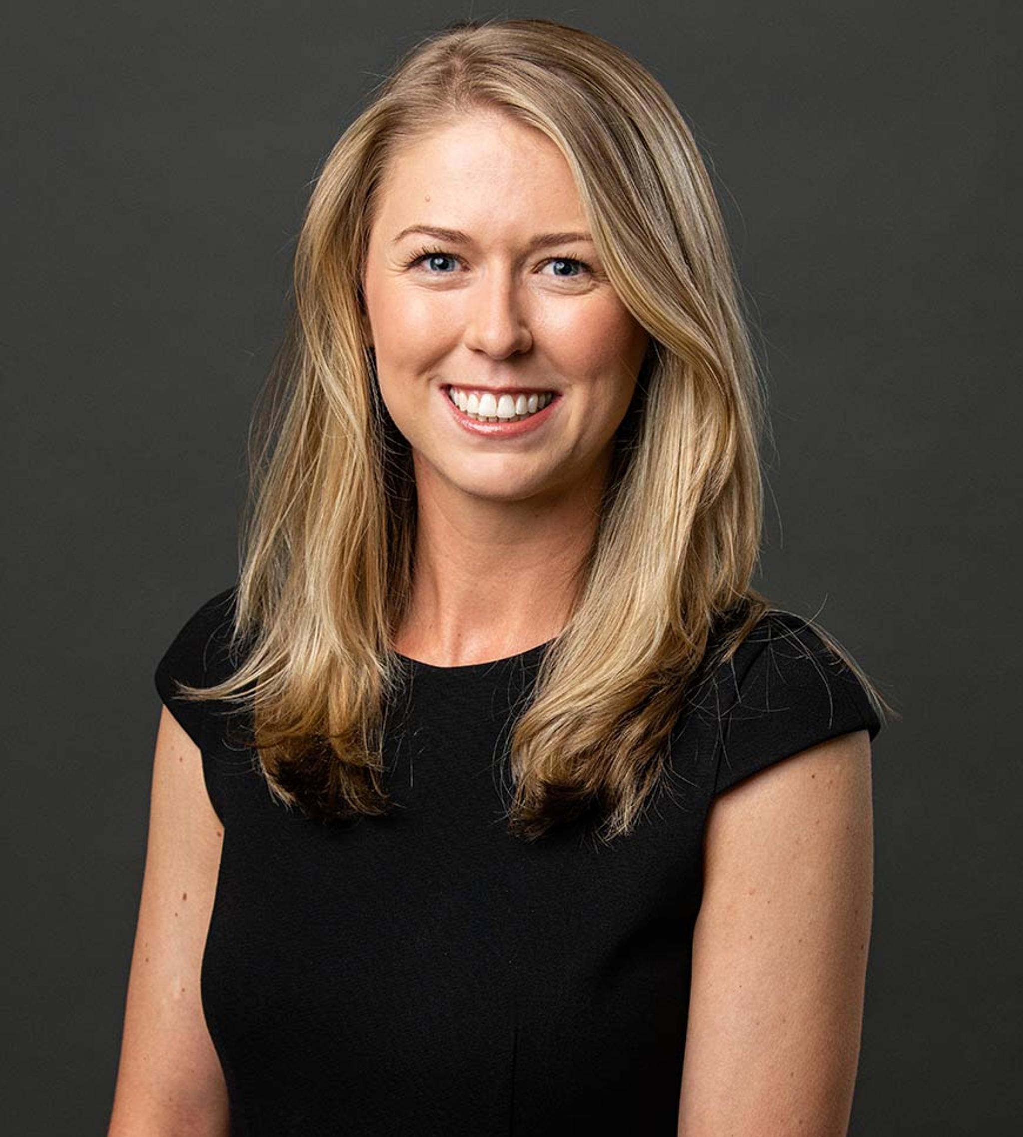Professional headshot of a smiling woman with long blonde hair wearing a black top.