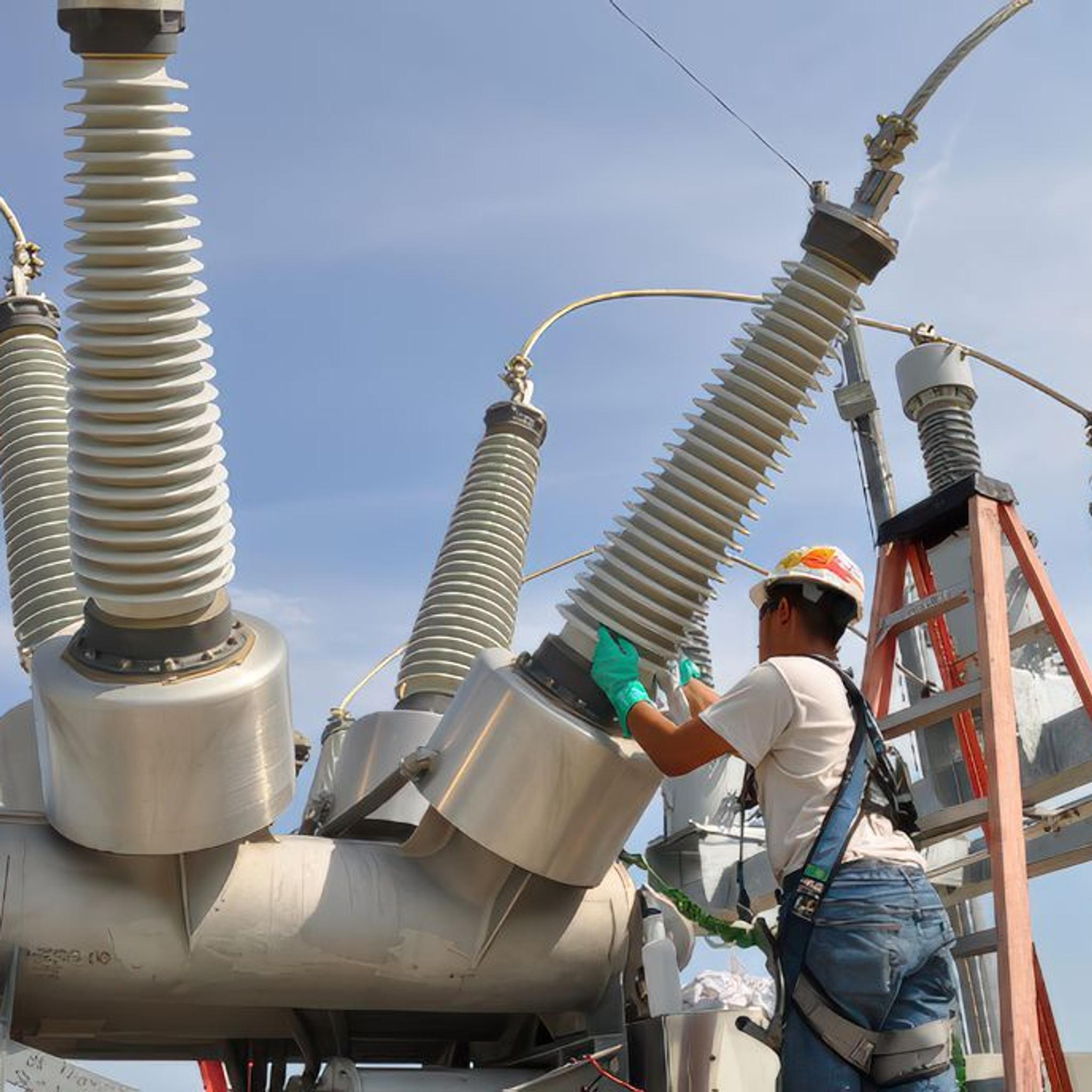 Technician services high-voltage switchgear bushings at an electrical substation.