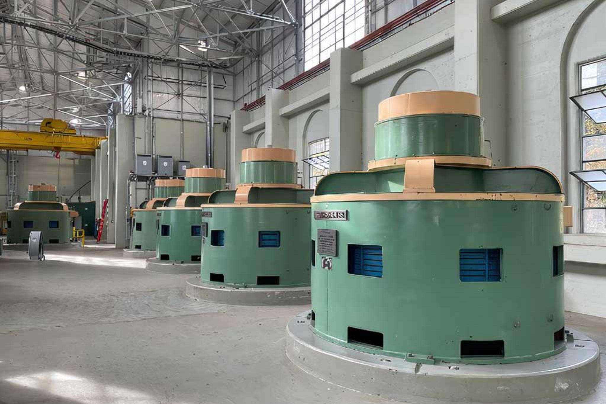 Large green generators line the floor of an industrial power plant.