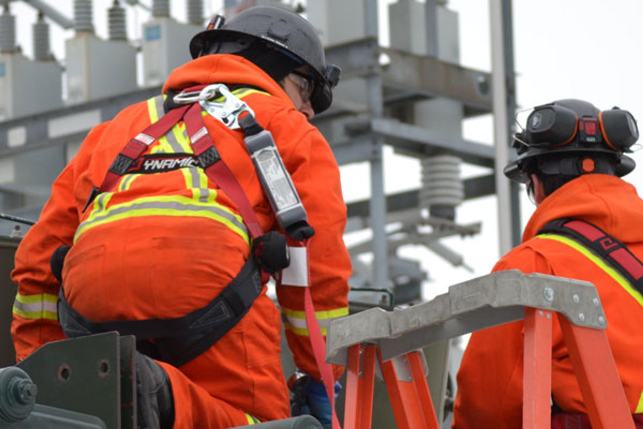 Technicians in safety gear service electrical equipment at a high-voltage substation.