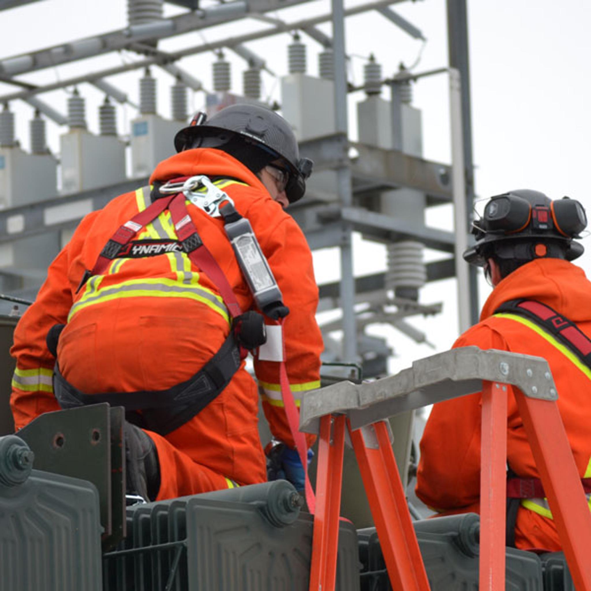 Technicians in safety gear service electrical equipment at a high-voltage substation.