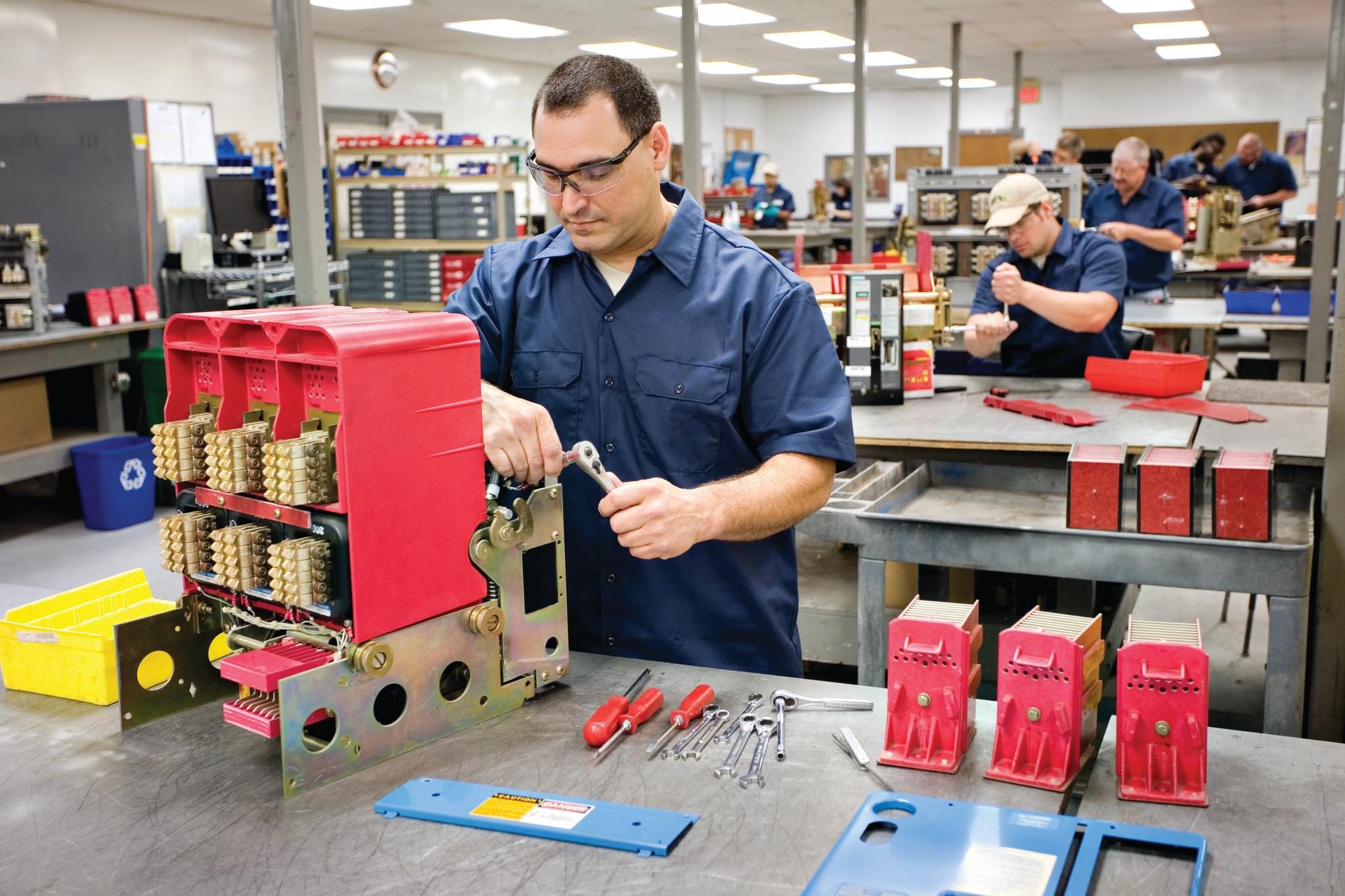 Technician uses a ratchet to service industrial switchgear in an electrical equipment repair shop.