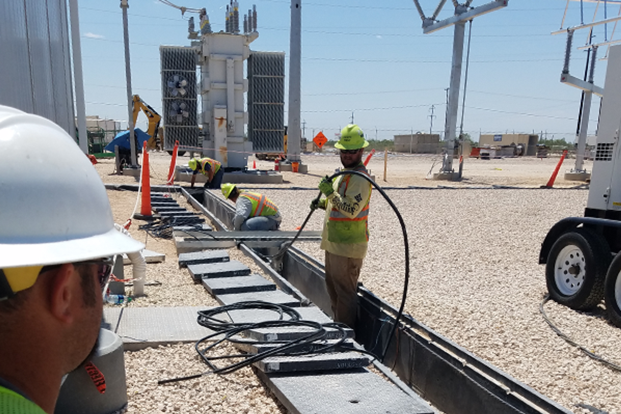 Técnicos instalan cables en una canaleta junto a un transformador de subestación eléctrica.