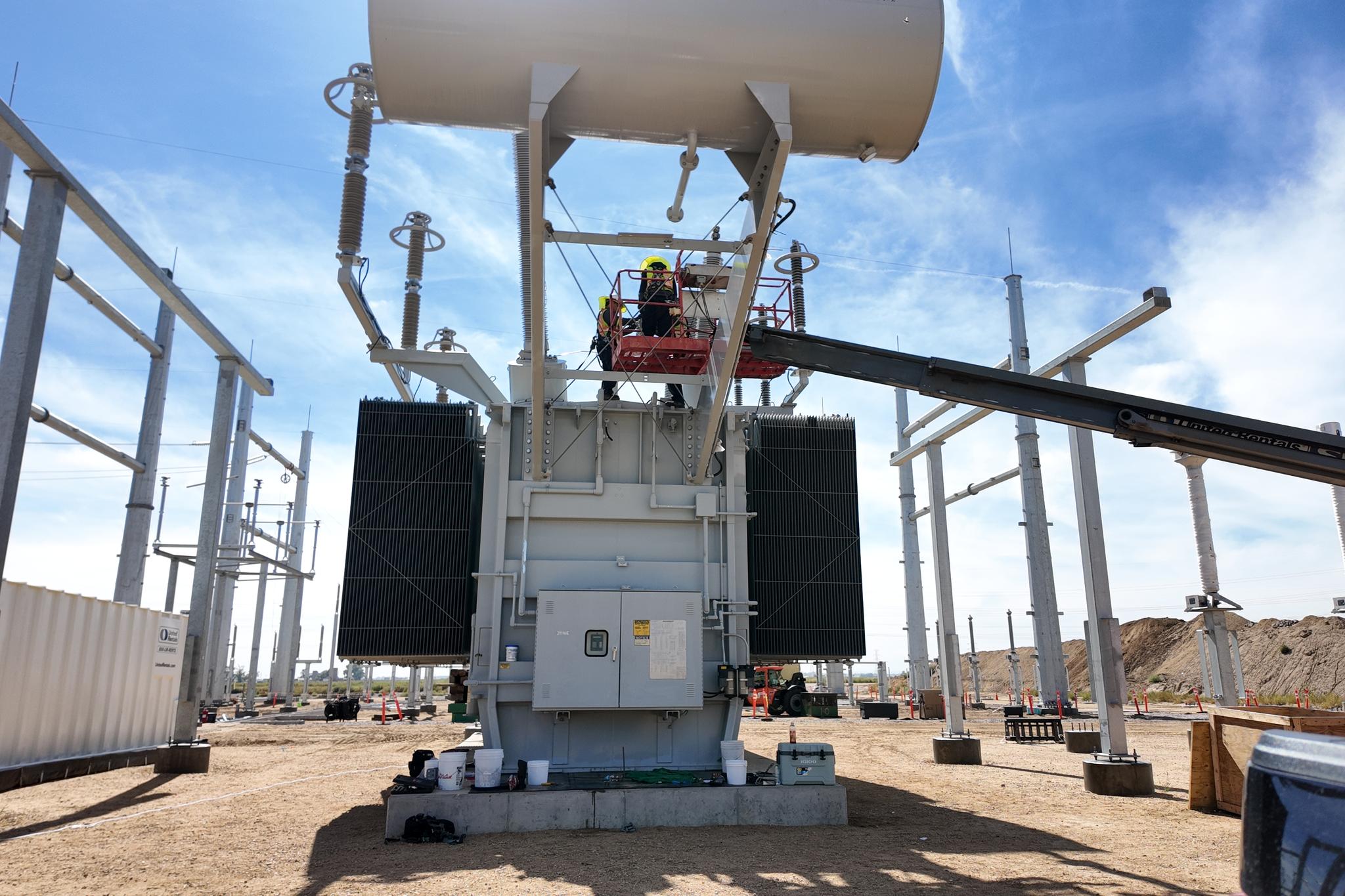 Technician in an aerial lift services a large power transformer at an electrical substation.