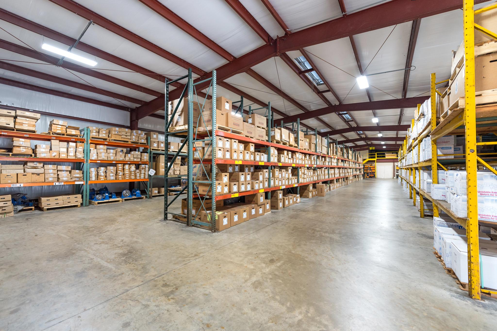 Warehouse racks hold boxed electrical equipment parts and motors along a wide aisle.