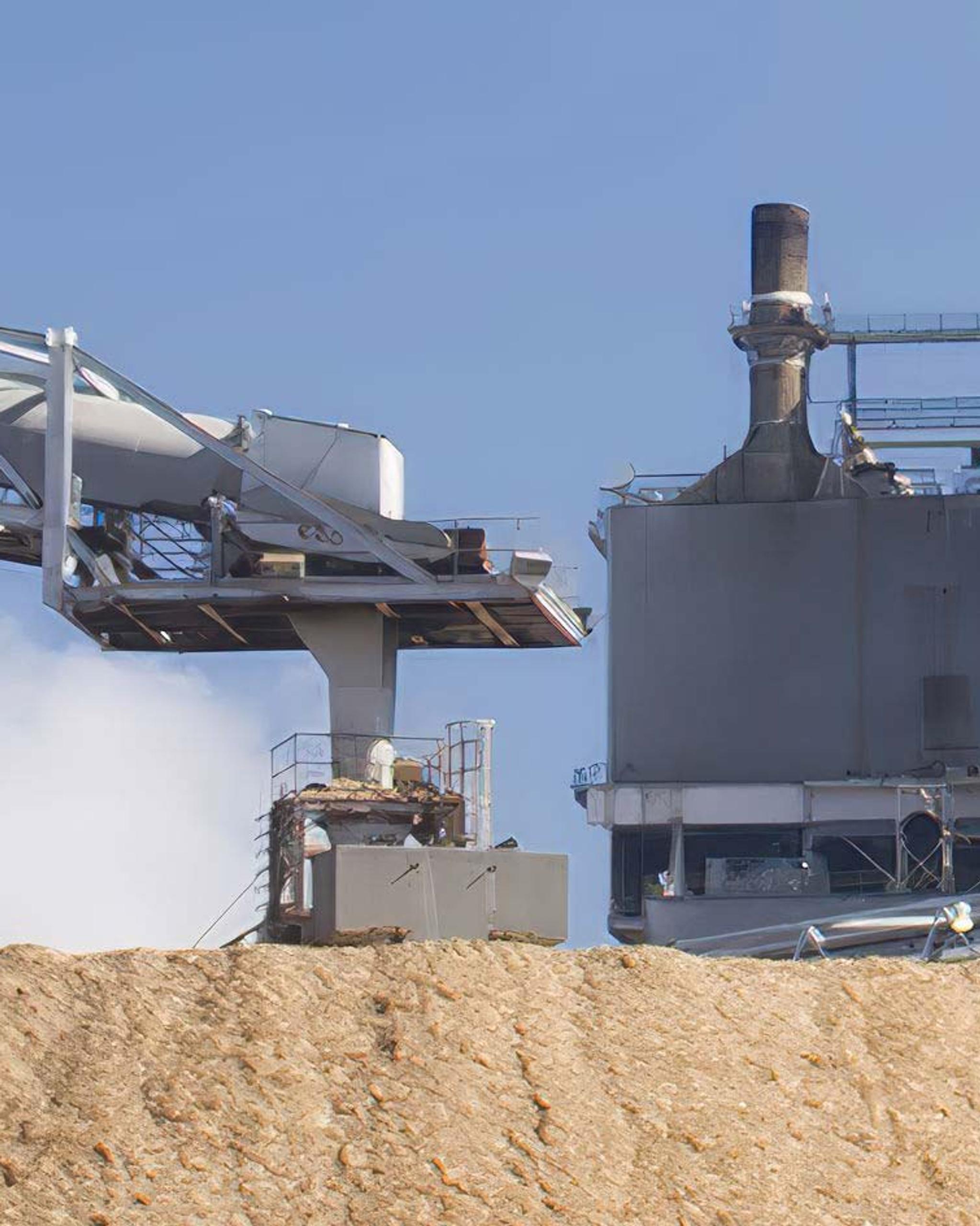 Equipos industriales dañados, con conductos y chimeneas deformados, en una planta con emisiones de vapor.