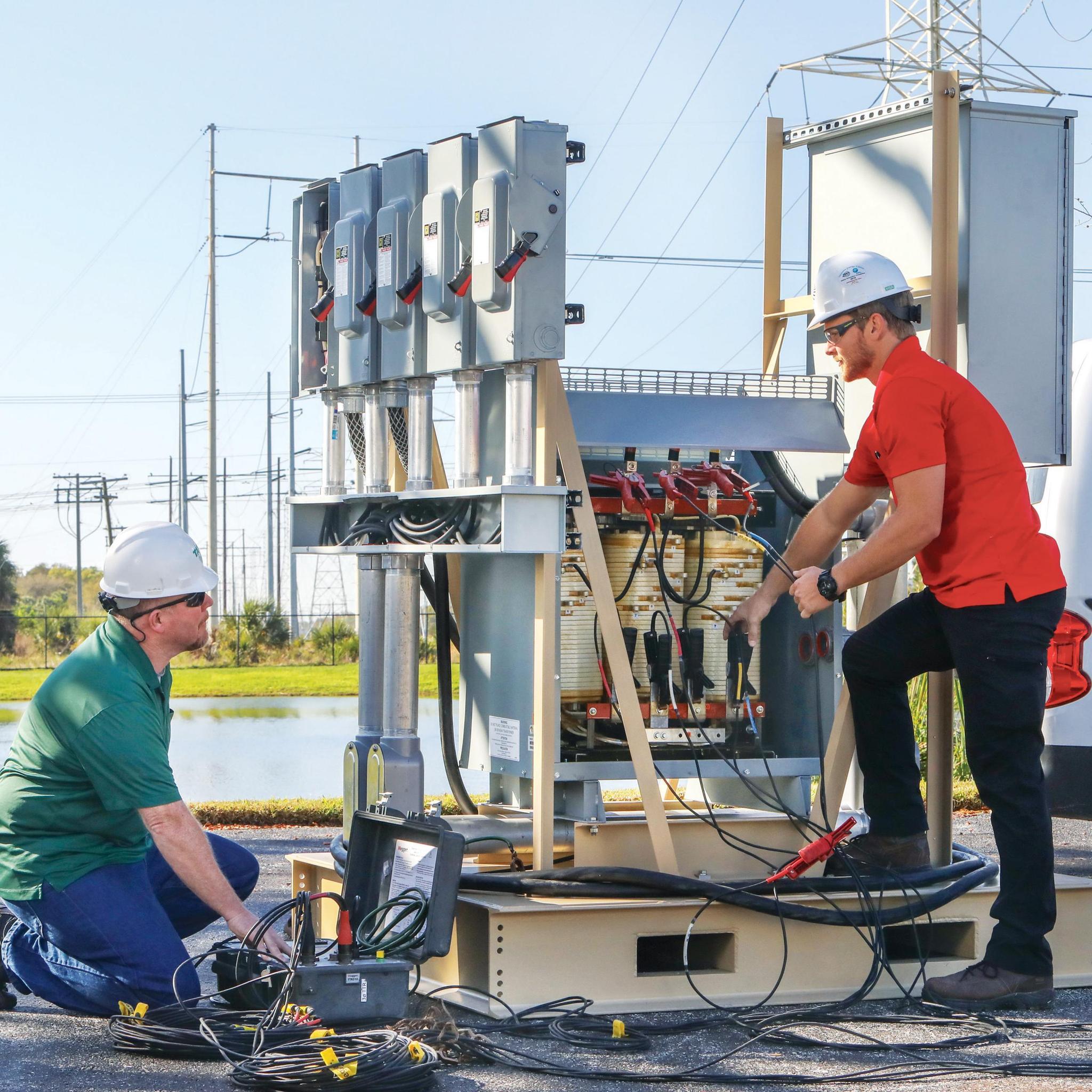 Deux techniciens testent un transformateur électrique avec des câbles et des appareils de mesure.