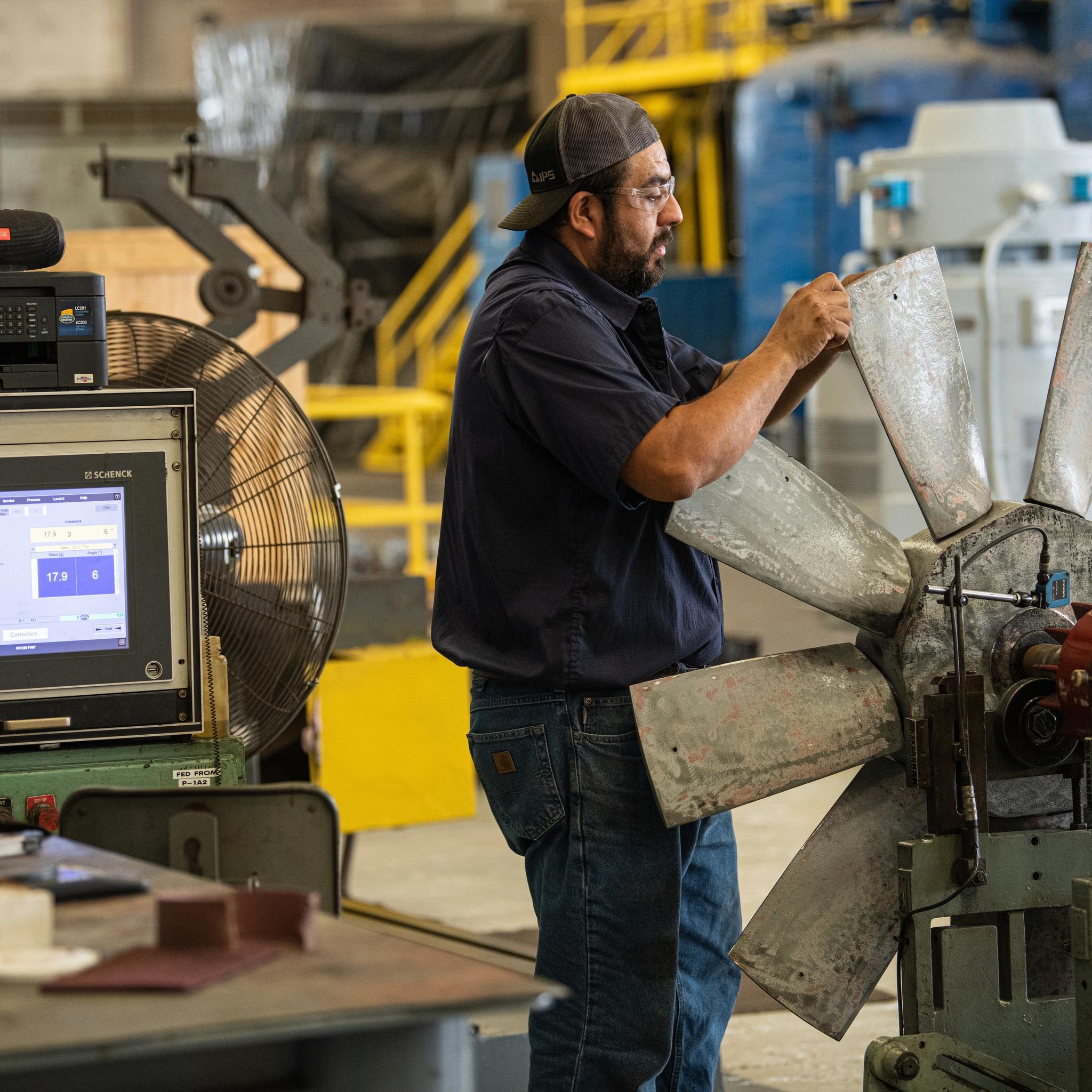 Technician balances a large industrial fan rotor using computerized testing equipment.