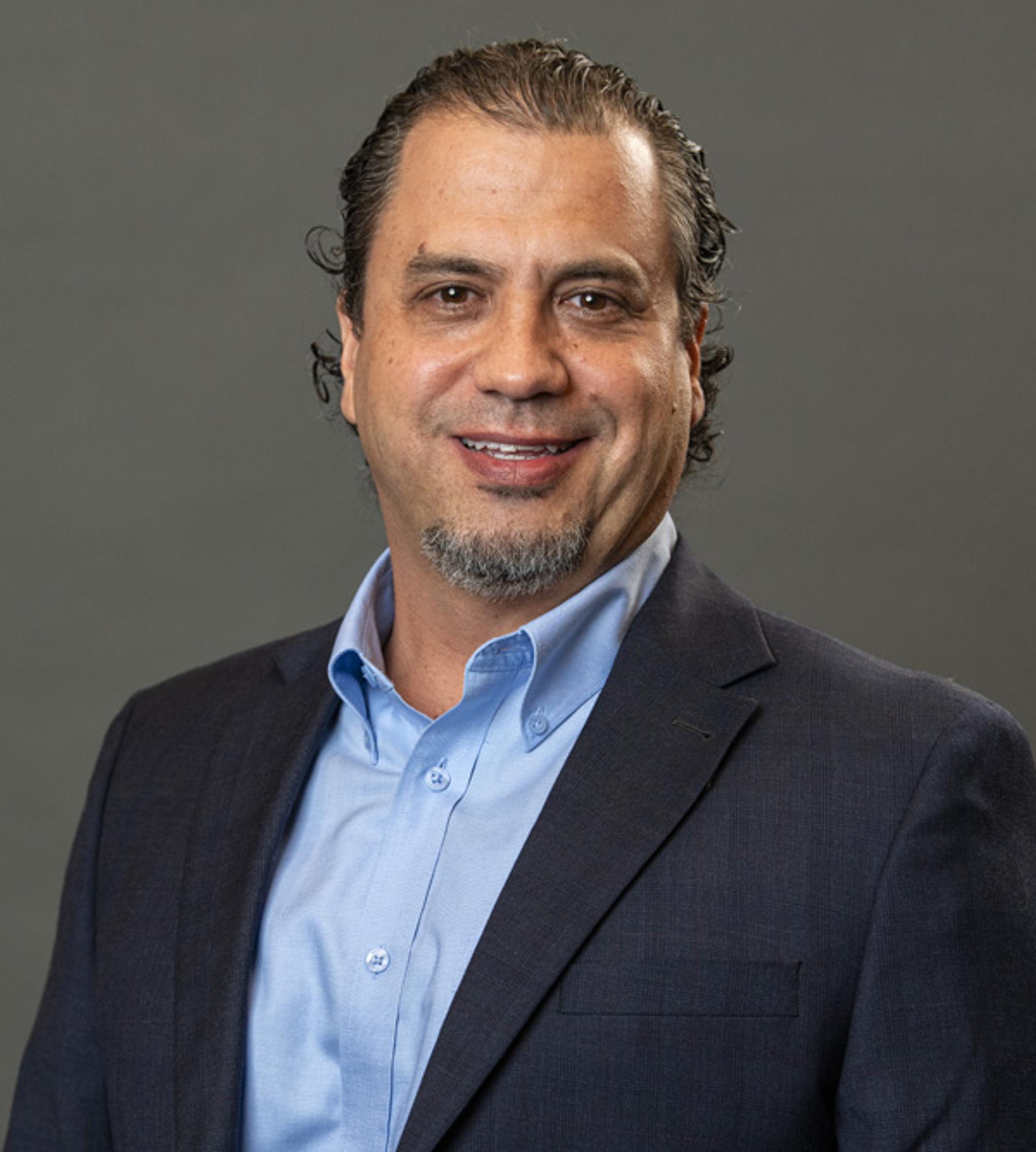 Portrait of a smiling man in a dark suit jacket and light blue shirt.