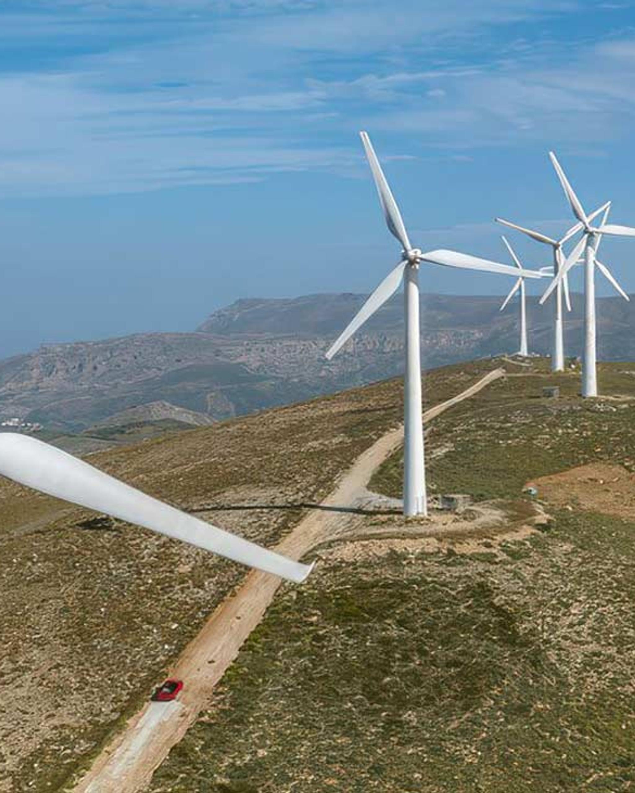 Éoliennes alignées sur une crête montagneuse, le long d’un chemin de terre.