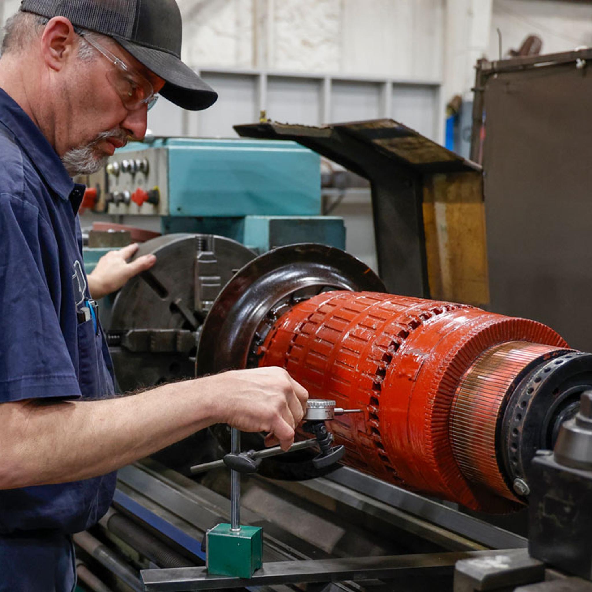 Técnico mide el rotor de un motor eléctrico industrial montado en un torno.