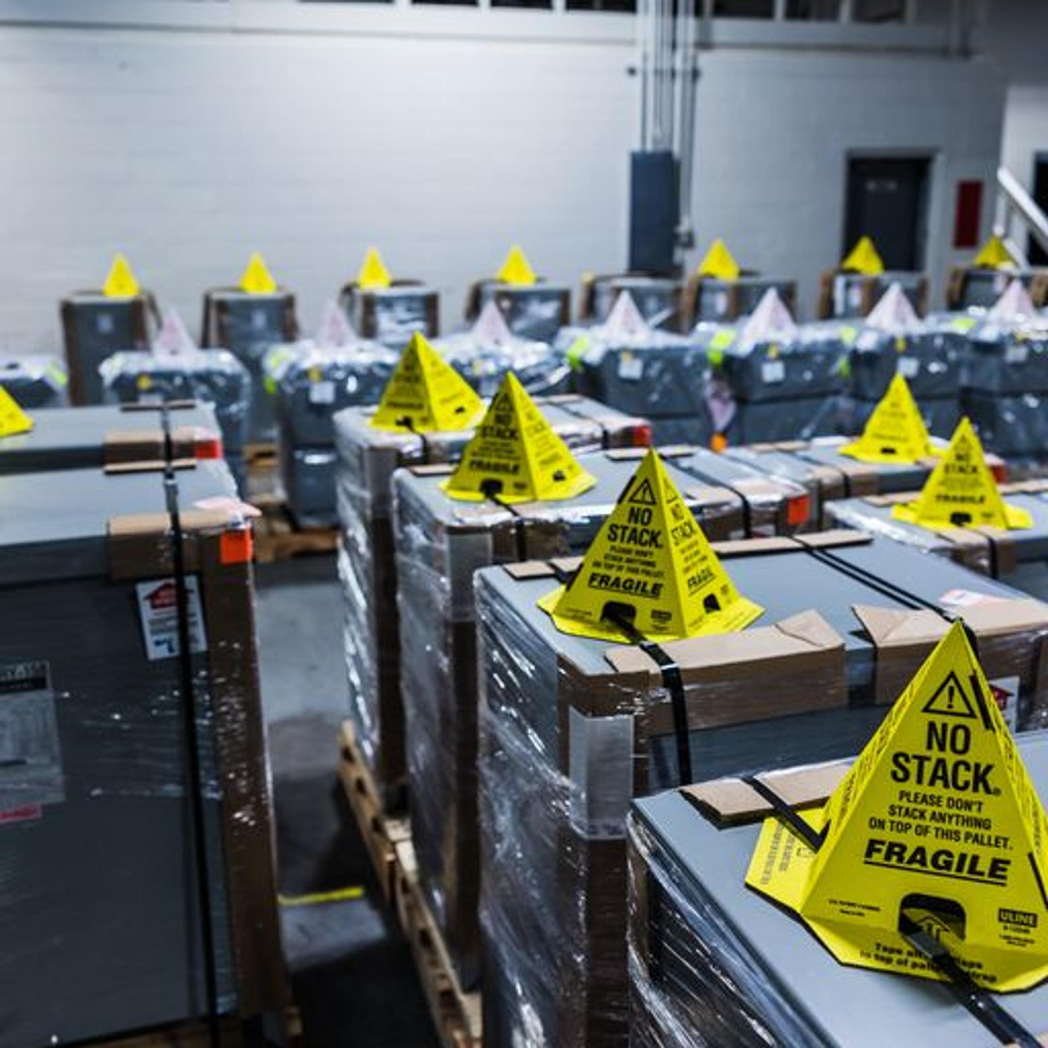 Palletized electrical equipment wrapped for shipping with yellow no-stack fragile warning cones.