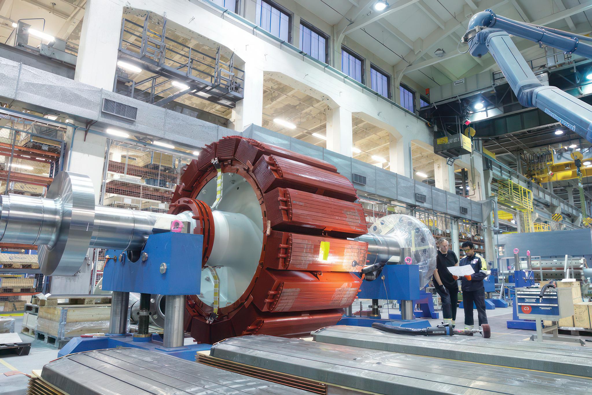 Deux techniciens inspectent le rotor d’un grand générateur électrique dans un atelier industriel.