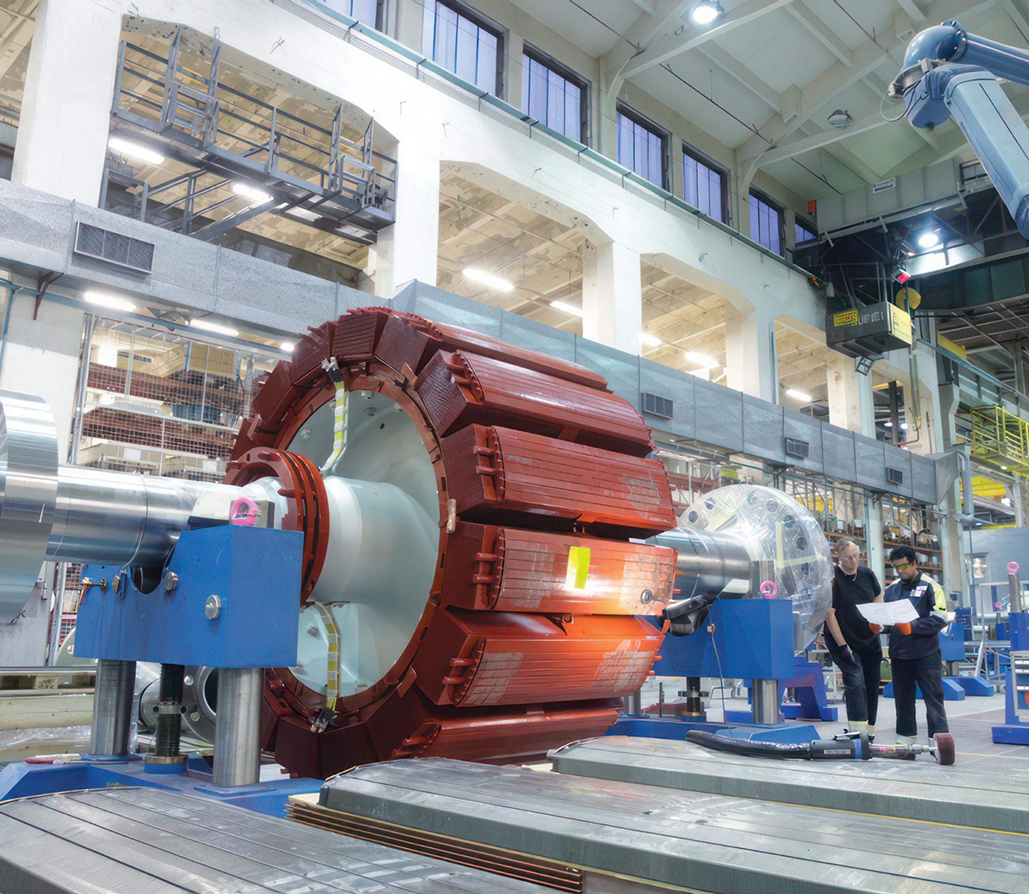 Deux techniciens inspectent le rotor d’un grand générateur électrique dans un atelier industriel.