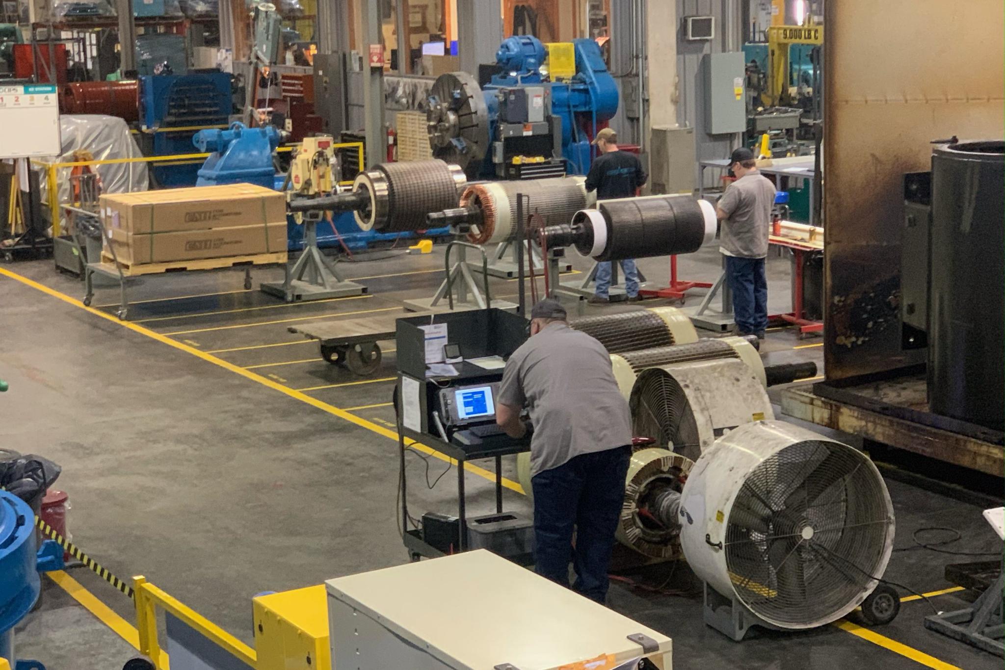 Technicians inspect and repair large motor rotors in an industrial service center.