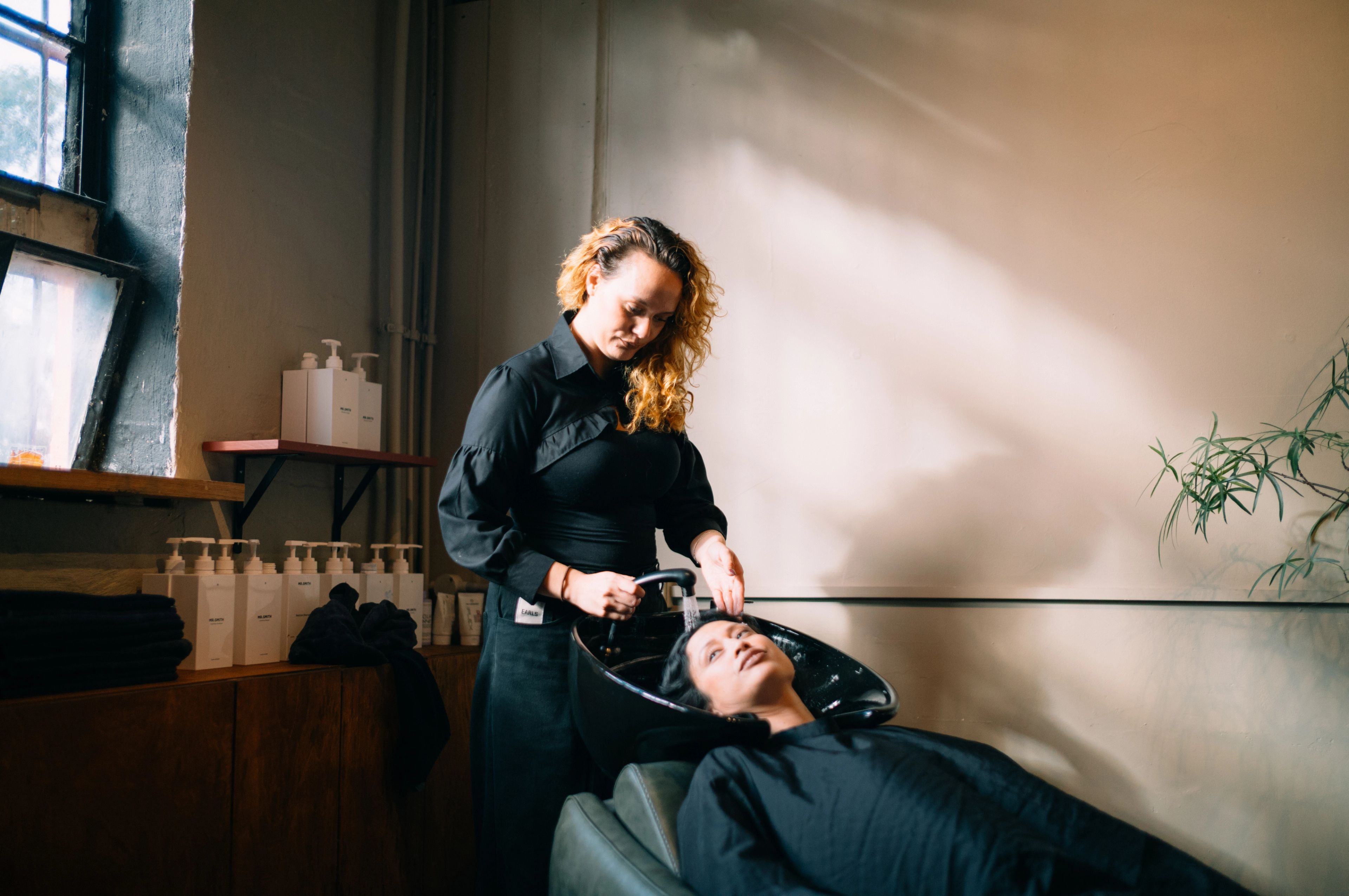A woman washing another woman's hair in a hair salon