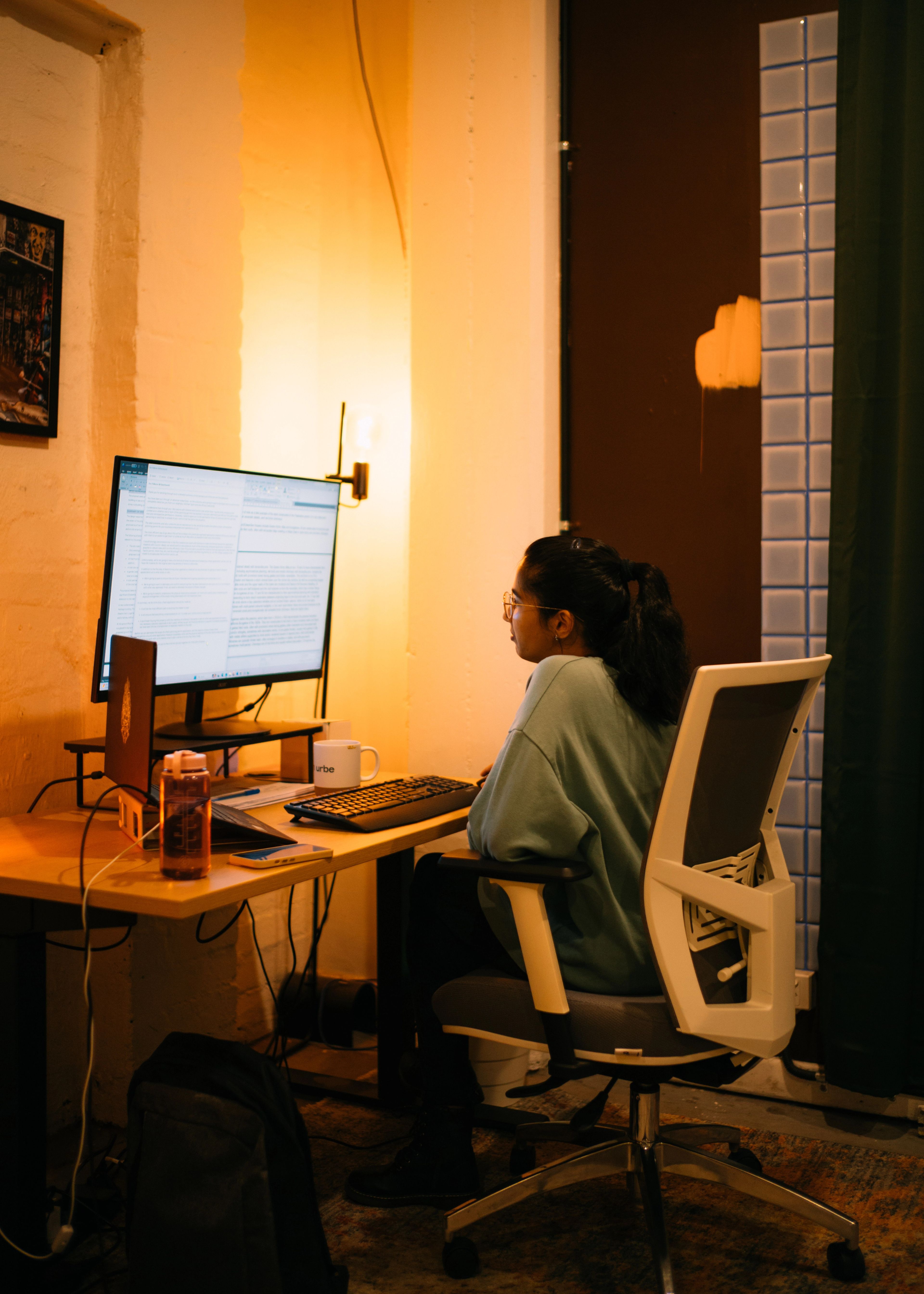 A devilishly stylish man, who may be french? Sat at a desk with a large colourful monitor.