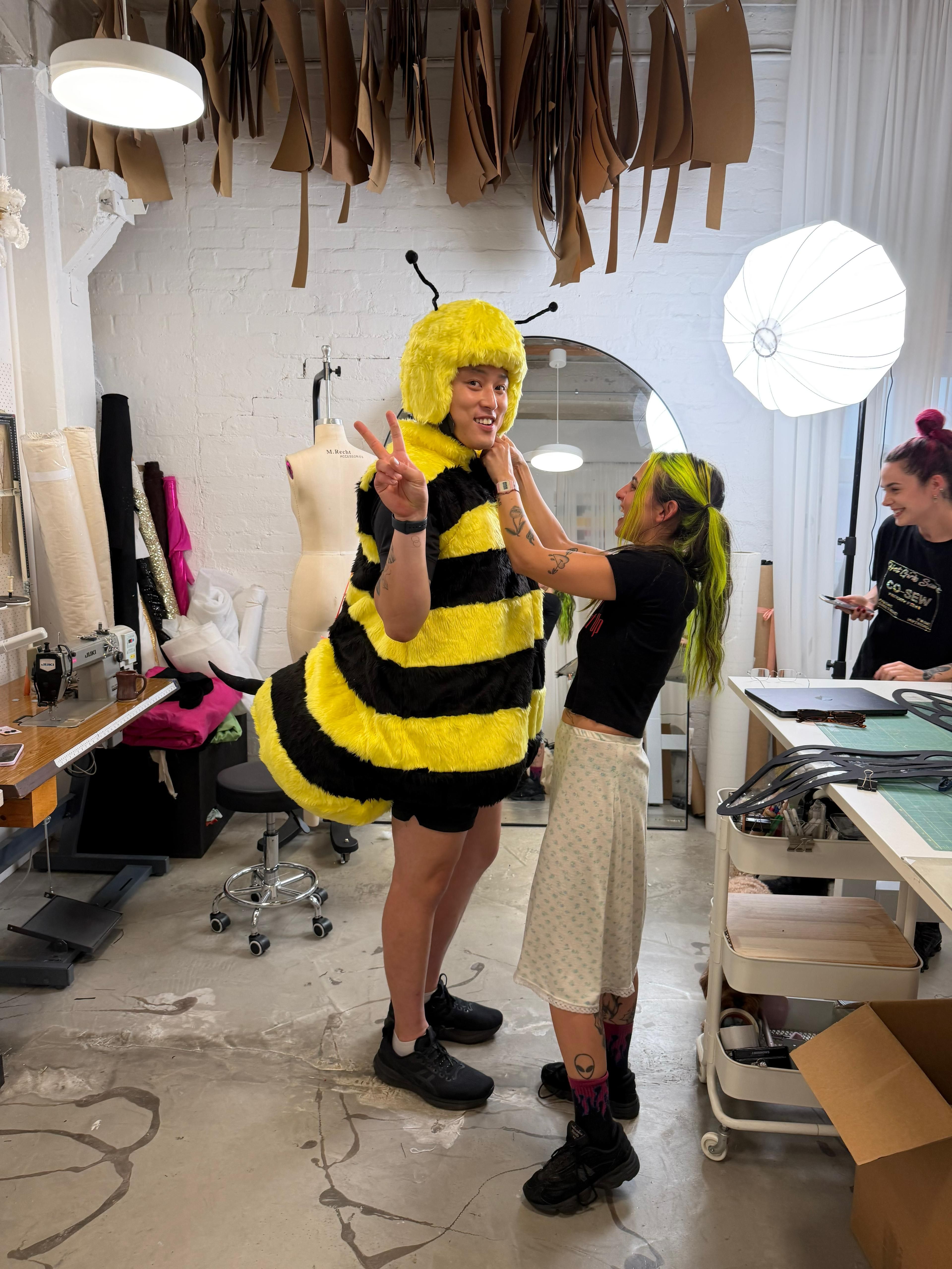 A fabulous man being fitted into a bee suit by two designers