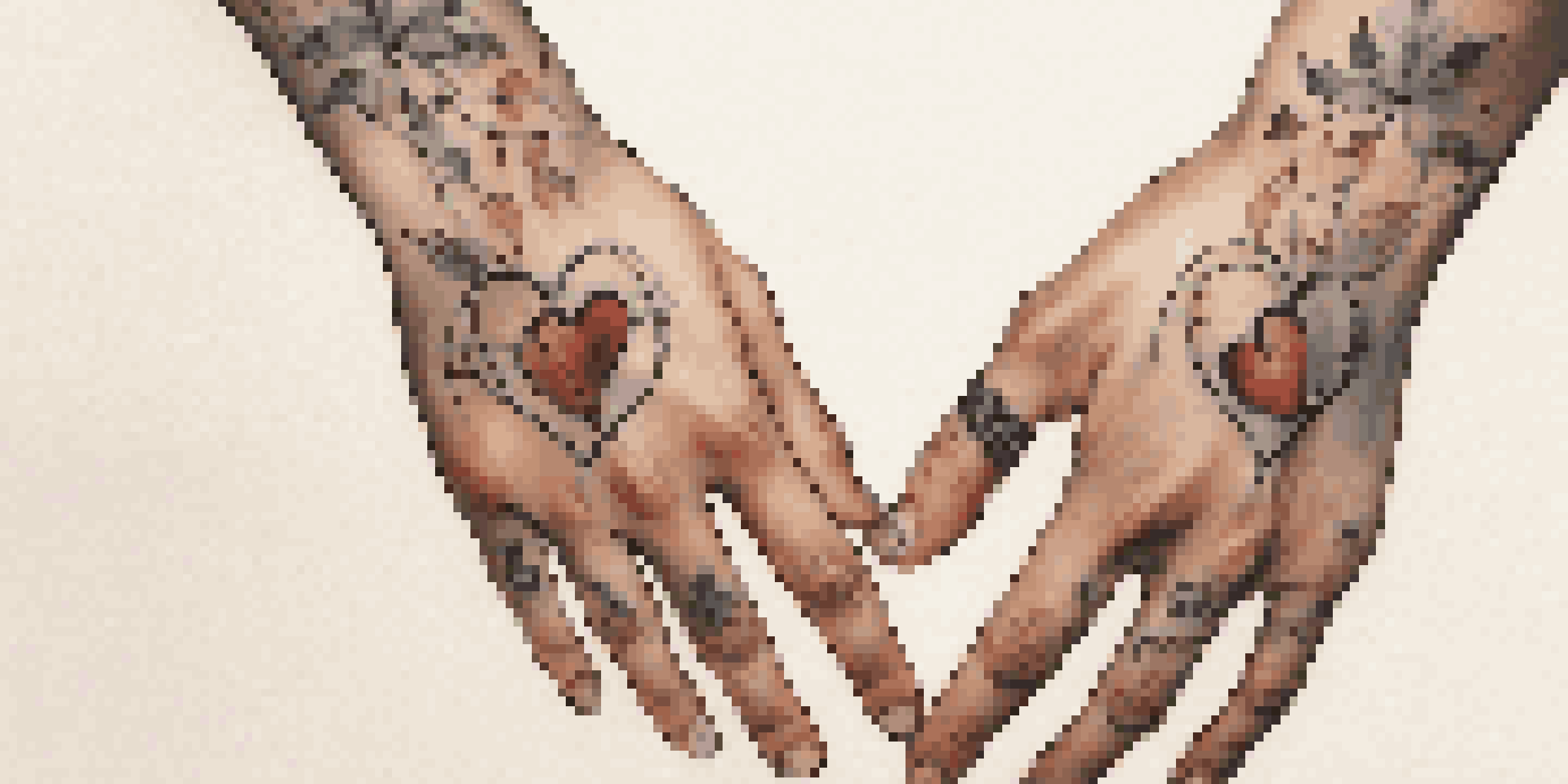 Close-up of two hands holding each other with matching small heart tattoos, displaying a warm and intimate connection.