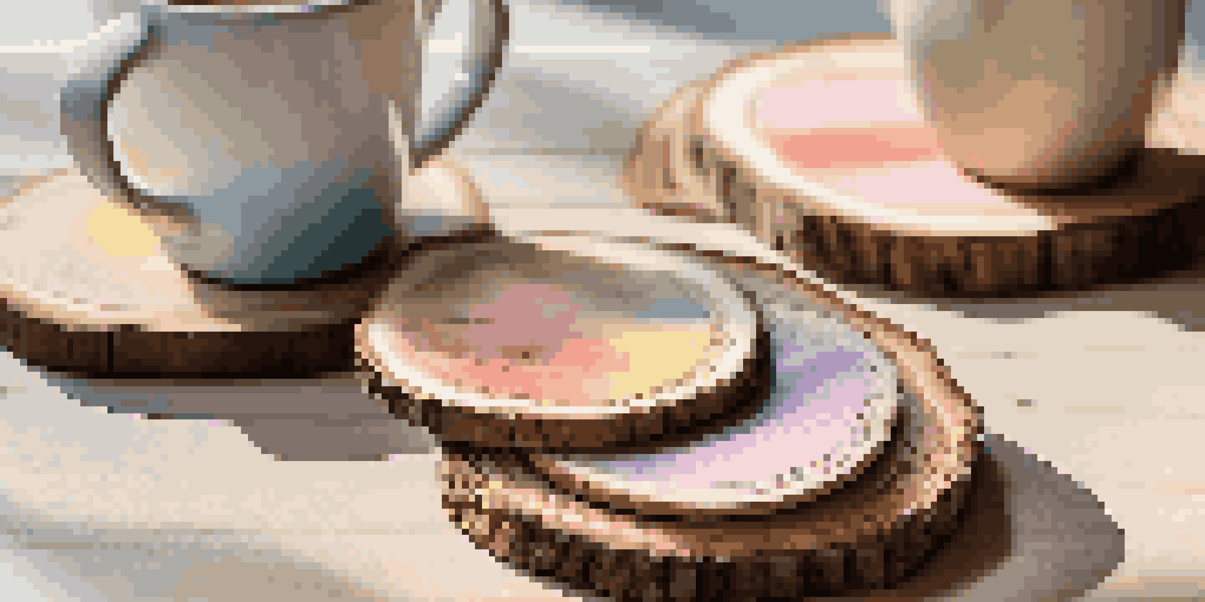 A set of colorful DIY coasters made from wood slices with ceramic mugs on a wooden table, illuminated by soft sunlight.
