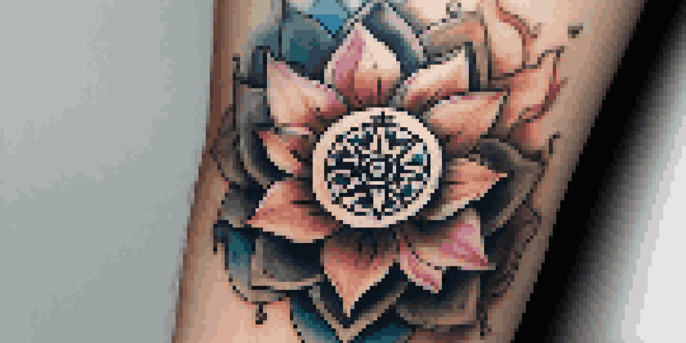 A close-up of a detailed tattoo showing a lotus flower and a compass on a forearm, illuminated by warm light.