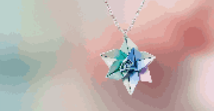 A close-up view of a colorful origami flower pendant on a silver chain, with intricate paper folds and a soft background.