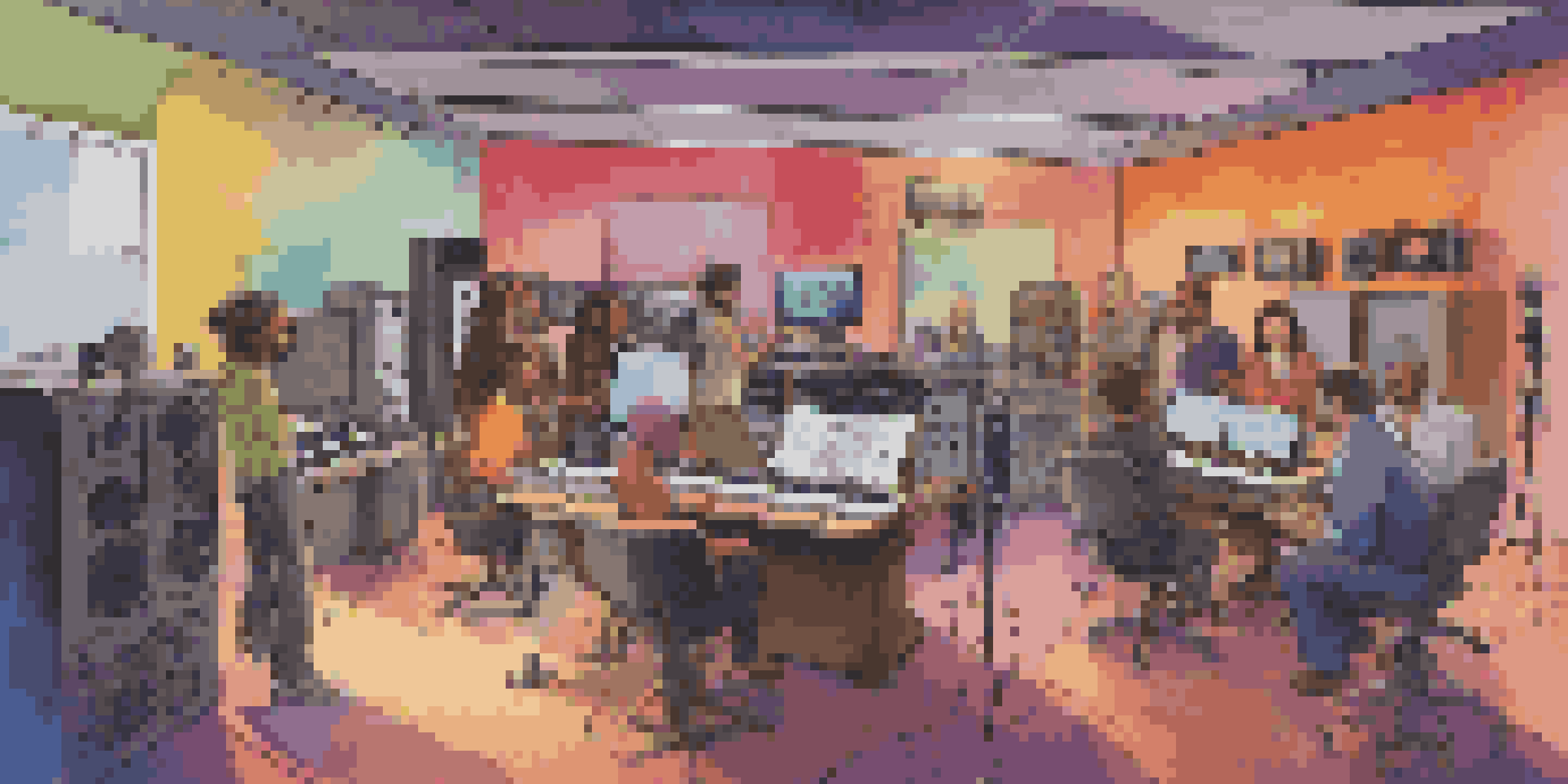 A modern recording studio with diverse voice actors discussing ideas around a large table filled with script pages and tablets.