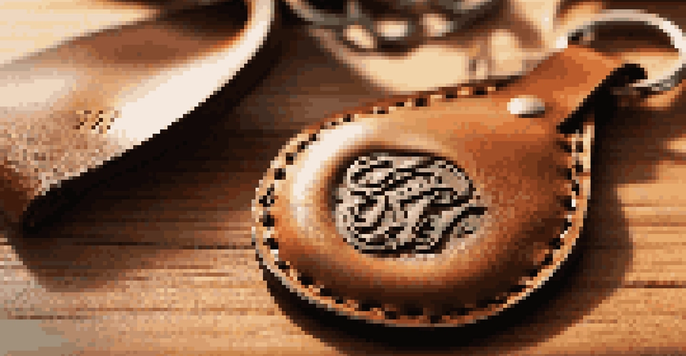 A detailed view of a leather keychain with personalized monogram, displayed in a rustic environment with crafting tools in the background.