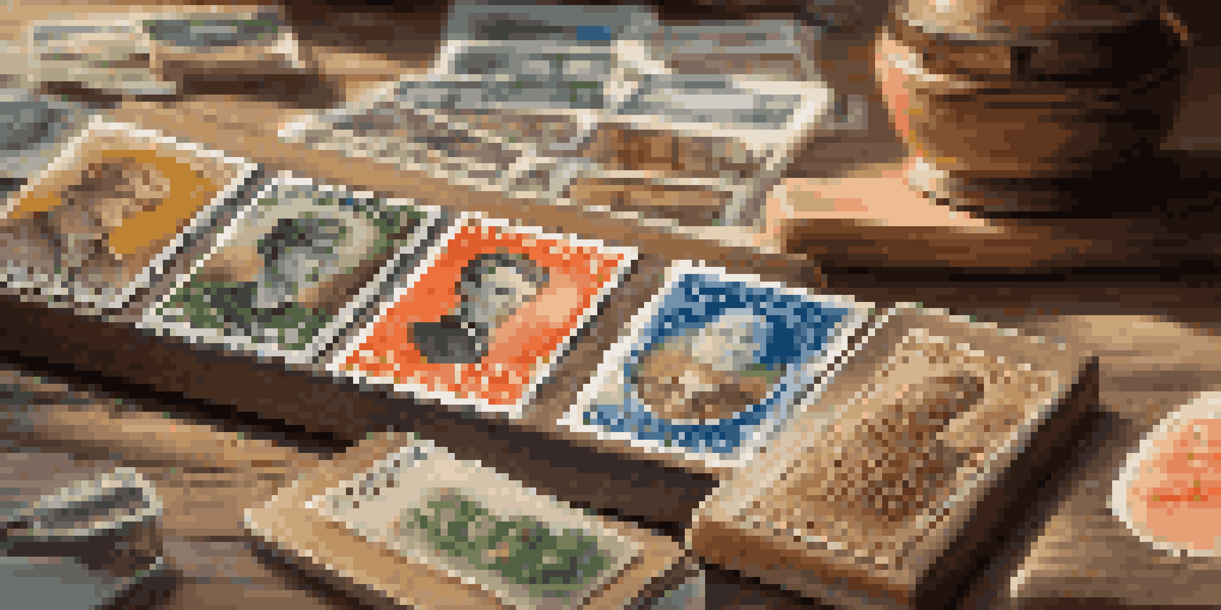 A detailed view of vintage stamps on a wooden table with a magnifying glass beside them, illuminated by sunlight.