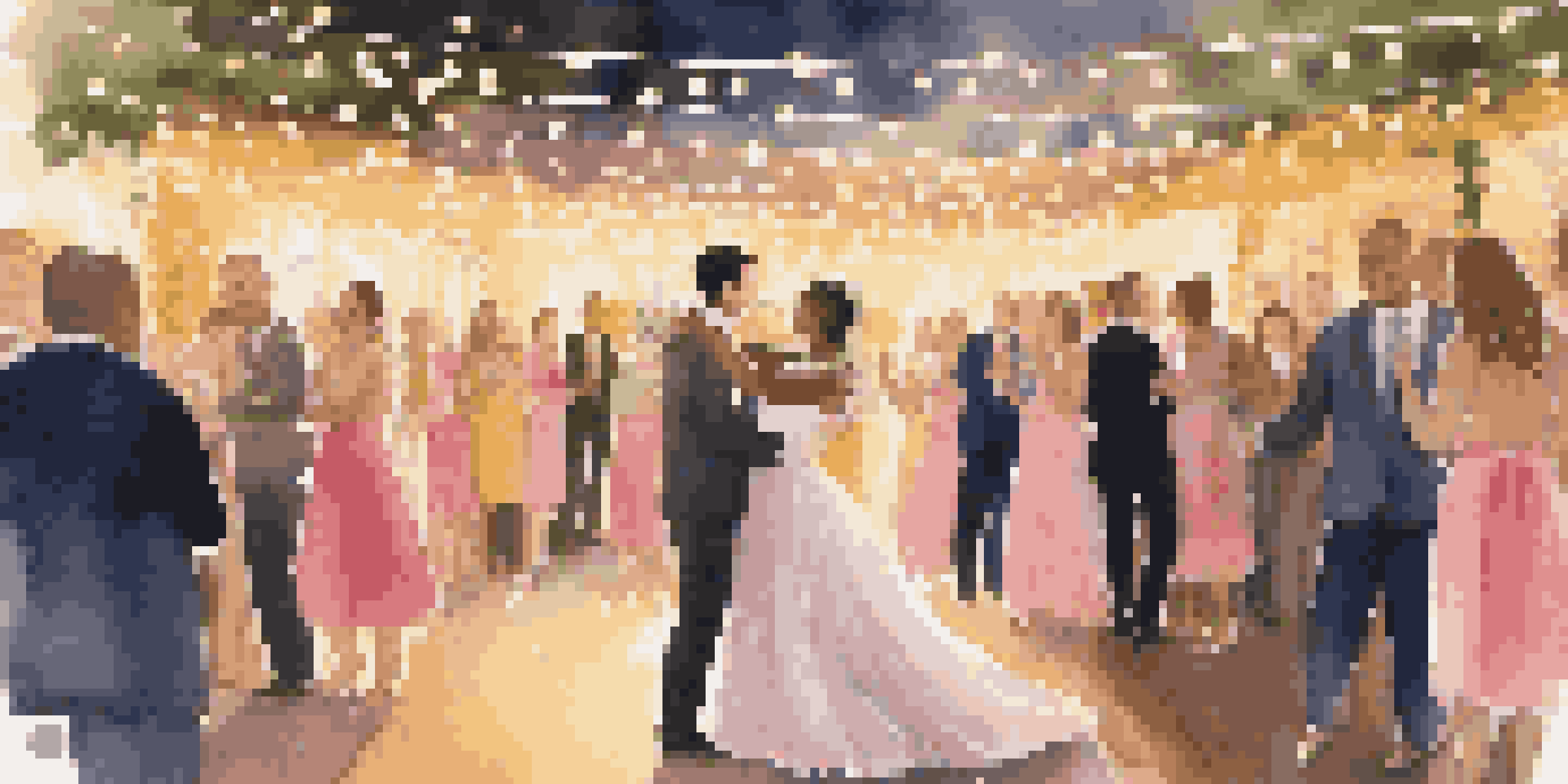 A happy couple dancing at their wedding under fairy lights, with blurred guests in the background.