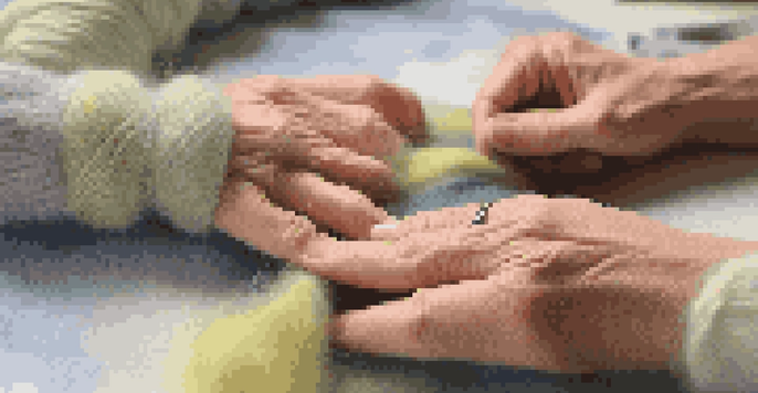 Hands demonstrating the felted join technique on wool yarn, with a soft-focus sweater in the background.