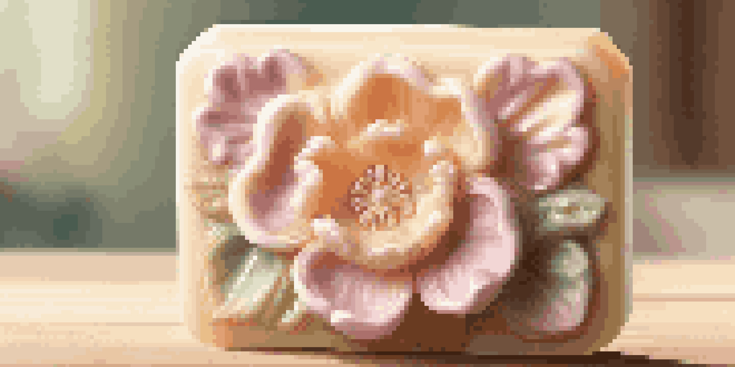 A close-up of a soap flower sculpture with intricate petal details on a wooden table illuminated by sunlight.