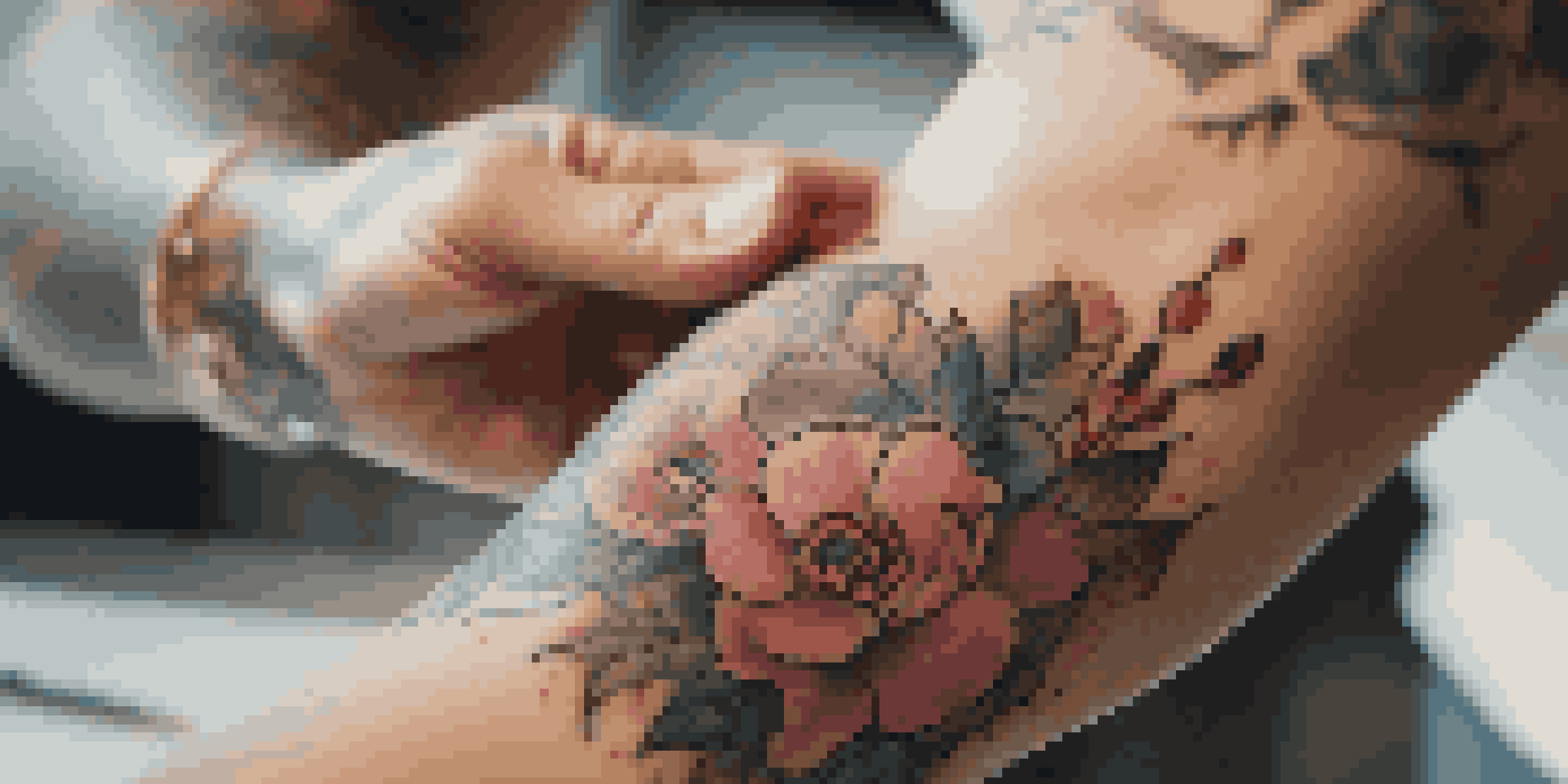 Close-up image of a tattoo artist tattooing a colorful floral design on a client's forearm, with tattoo tools in the background.
