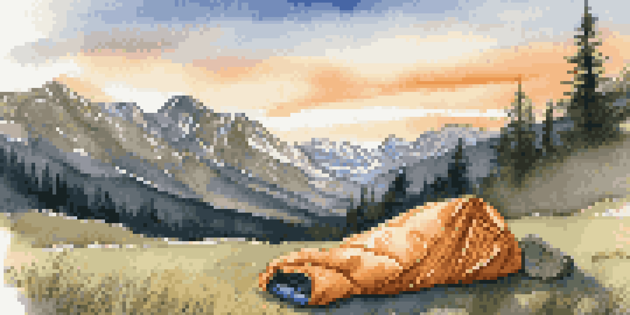 A close-up view of a down sleeping bag on a grassy campsite with mountains in the background during sunset.