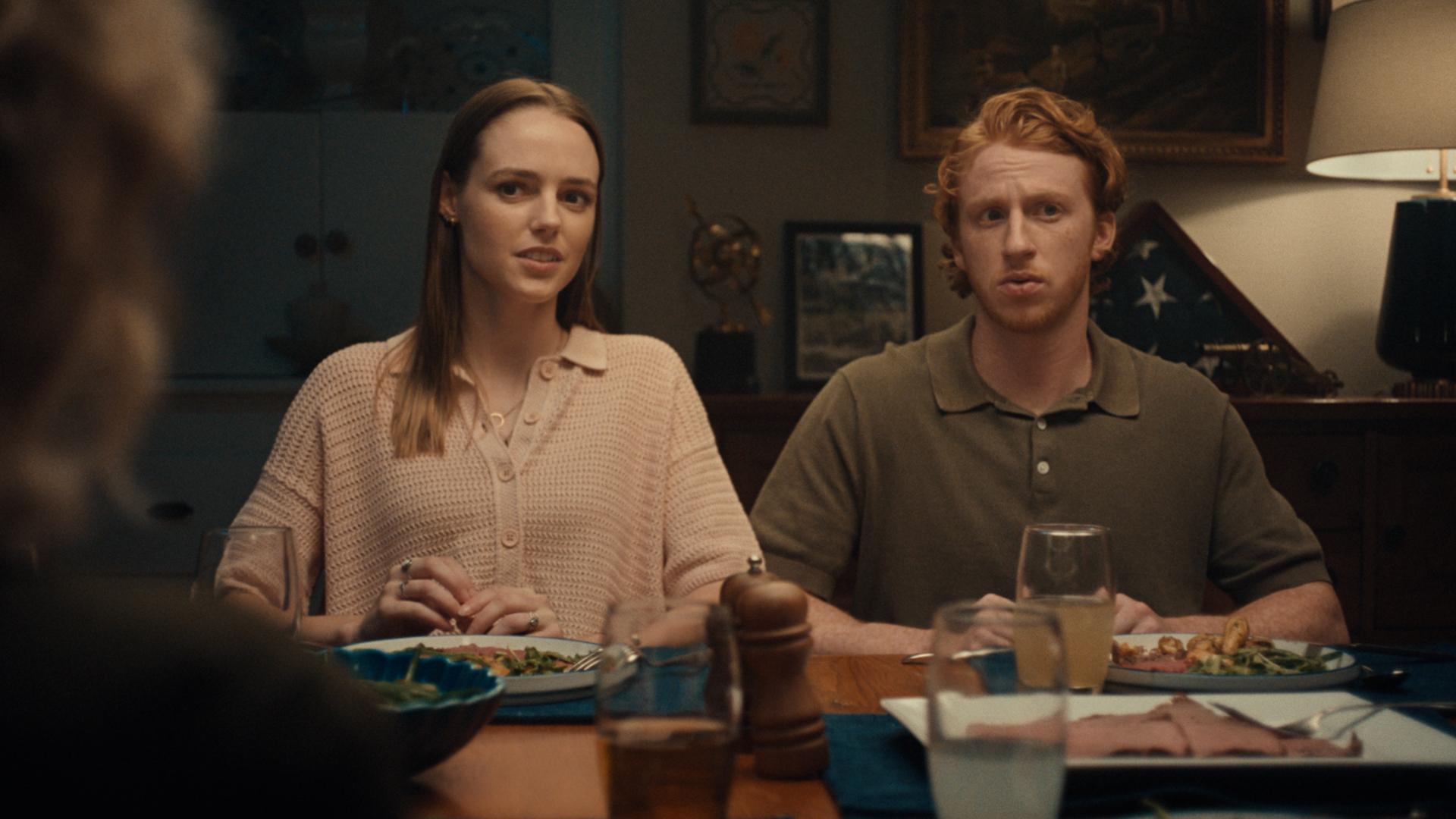 Two people sitting next to each other at dinner table with uncertain expressions