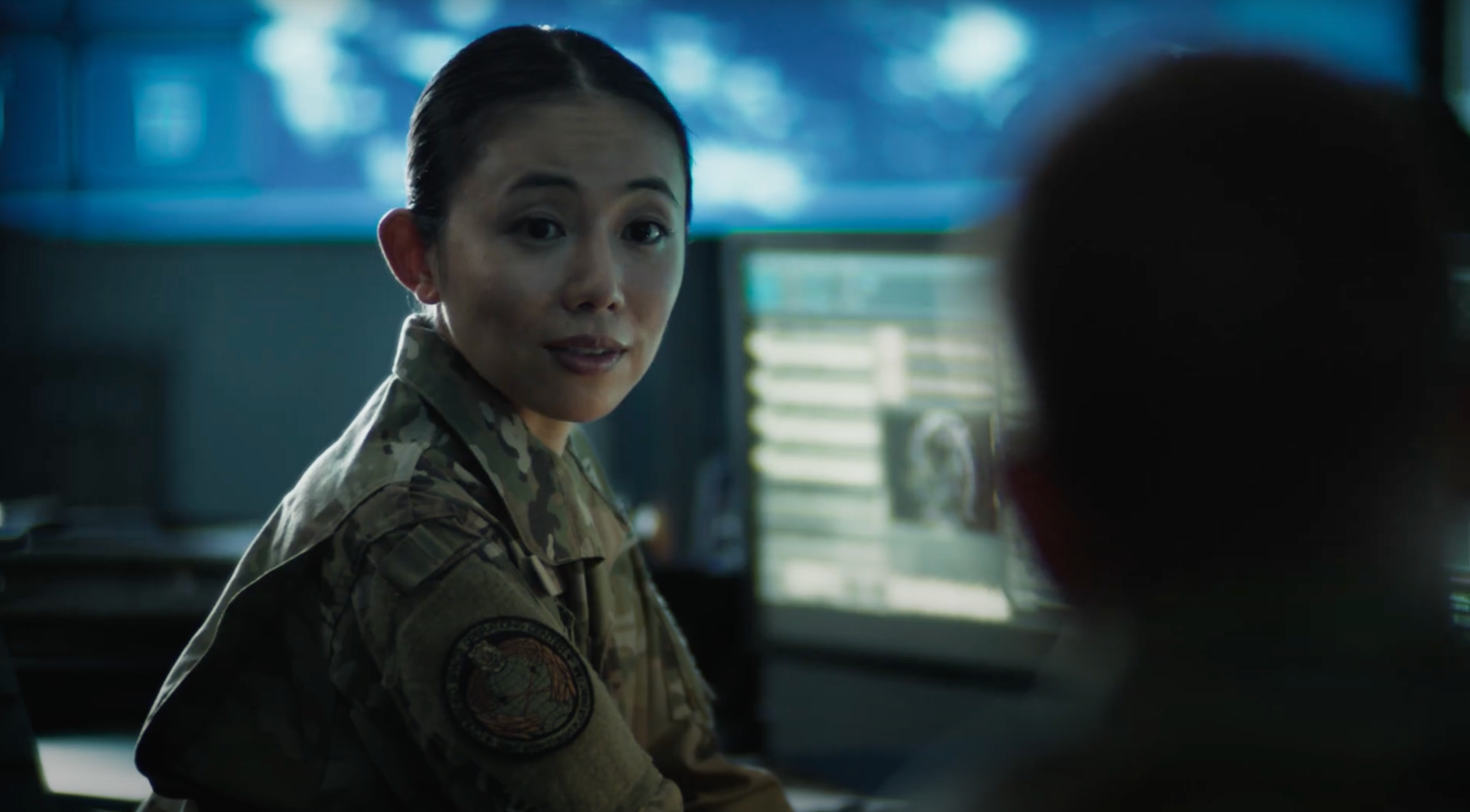 Military woman looking to camera in uniform at desk with screens behind her