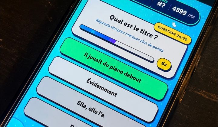 Un téléphone posé sur une table affiche une question musicale et les réponses proposées dans Vibzz.