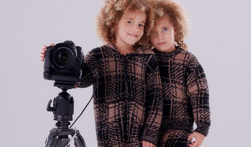 Two kids wear kids cozy knit while posing with a camera.